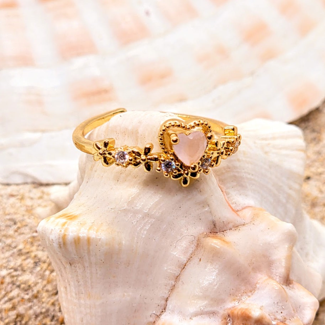Gold ring with a heart-shaped pink stone on a seashell