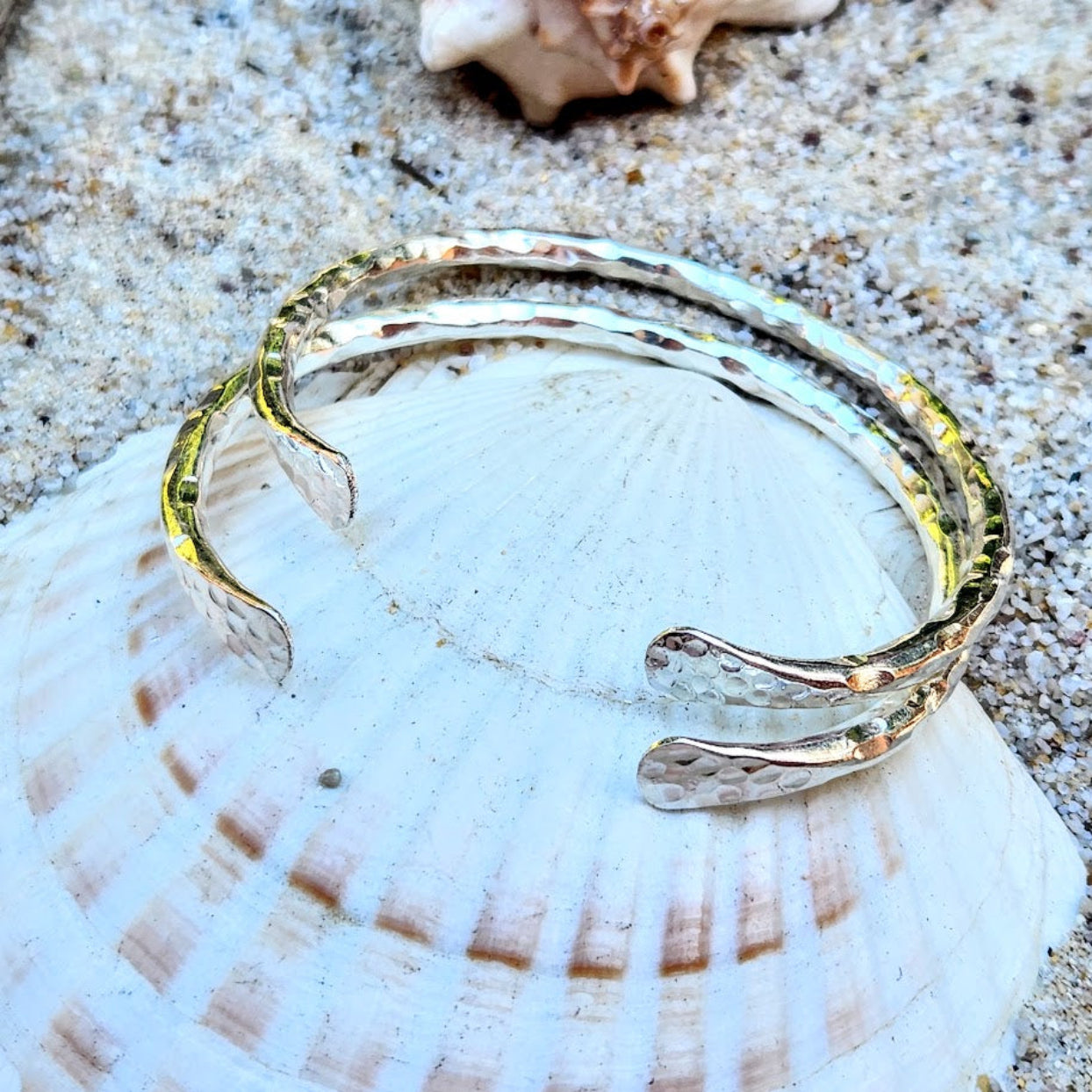 Silver bracelet on a seashell with sand in the background