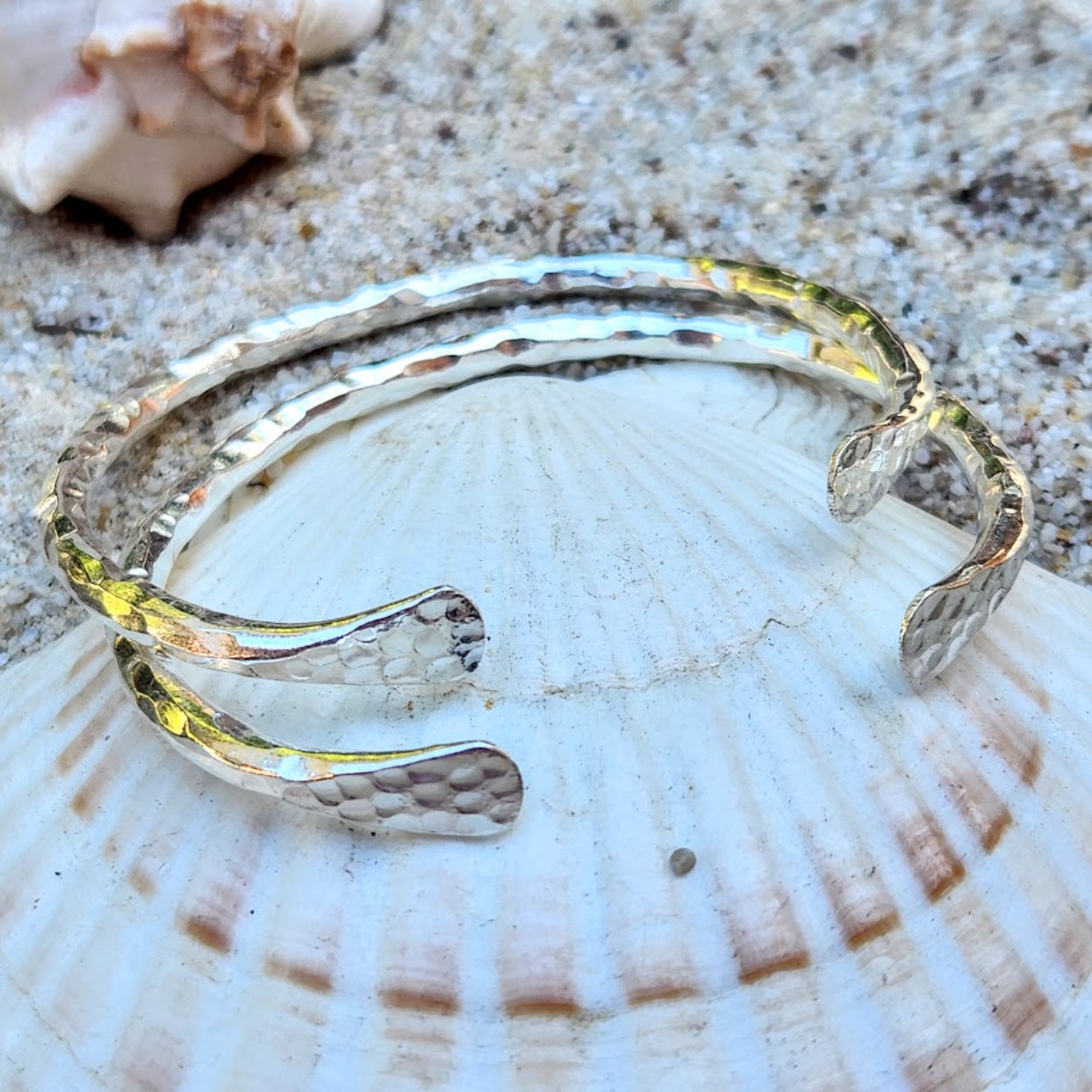Silver bracelet on a seashell with sand in the background
