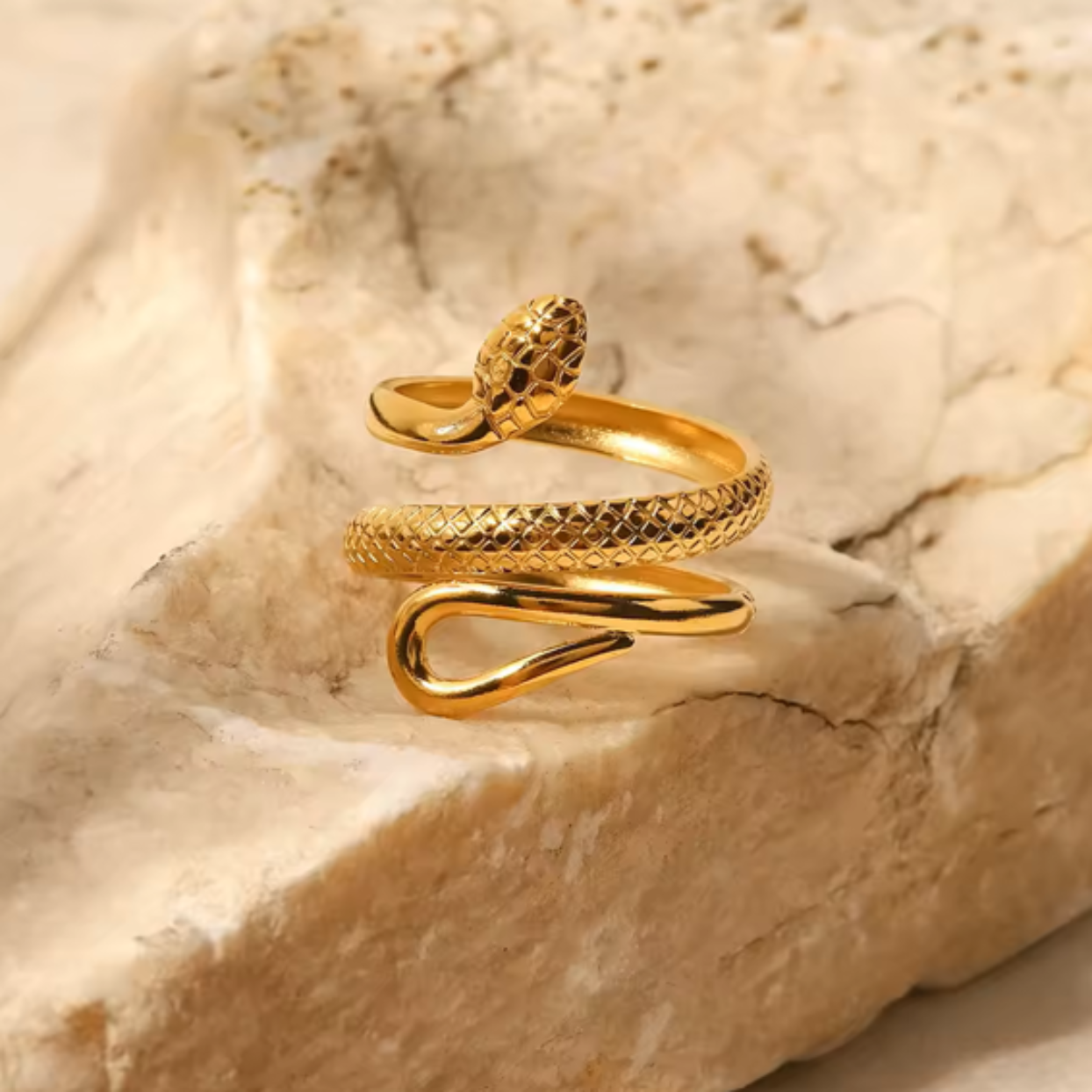 Gold snake-shaped ring on a textured stone surface