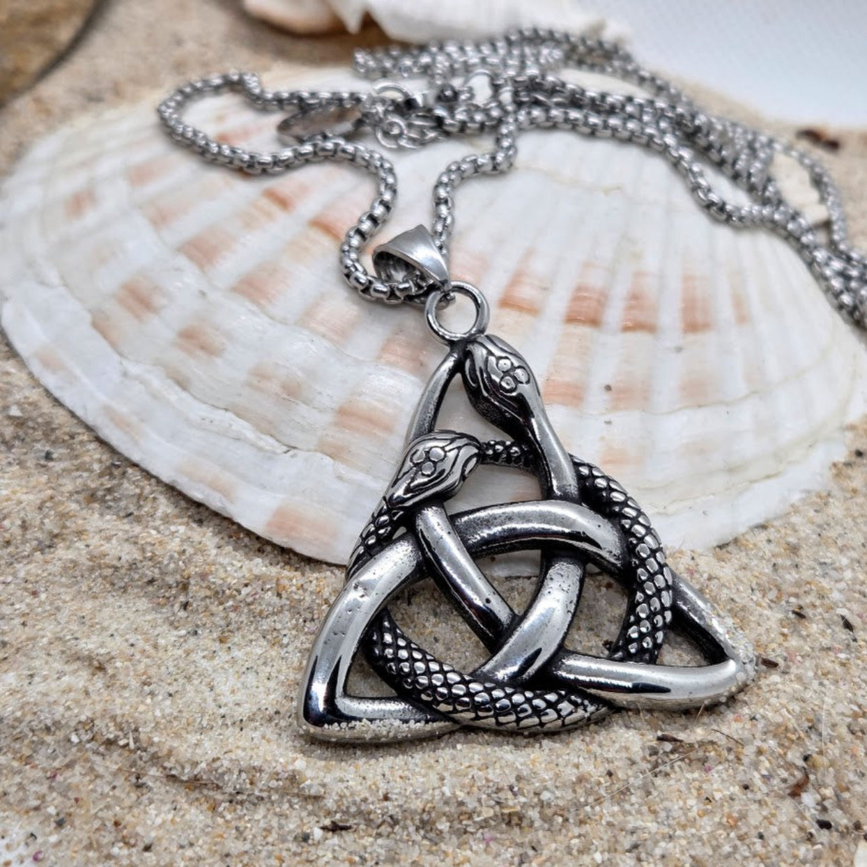 Silver necklace with a trinity knot pendant on sand and shell background
