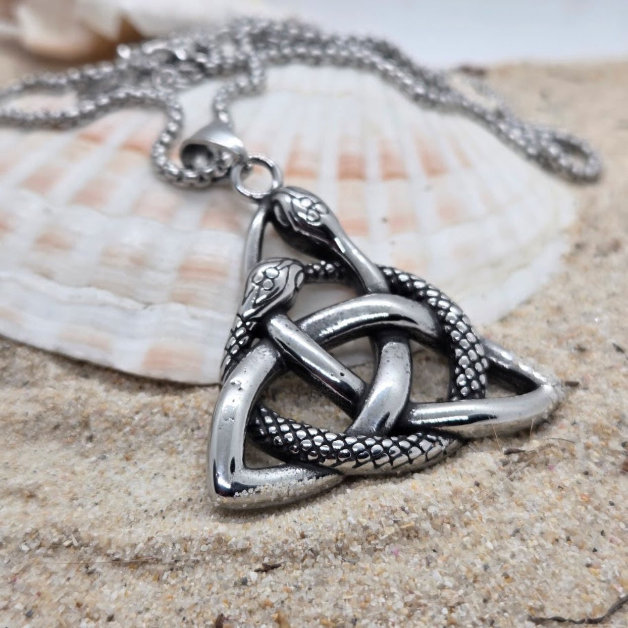 Silver triskele pendant on a chain with a shell in the background