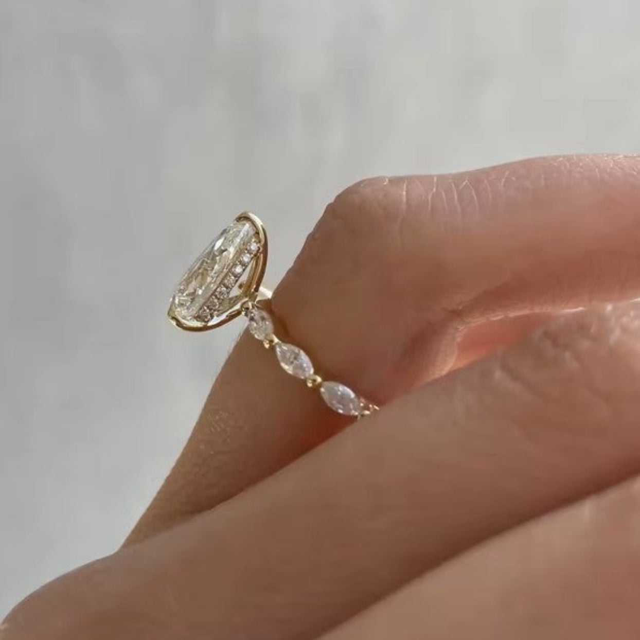 Gold ring with a large diamond on a finger against a neutral background