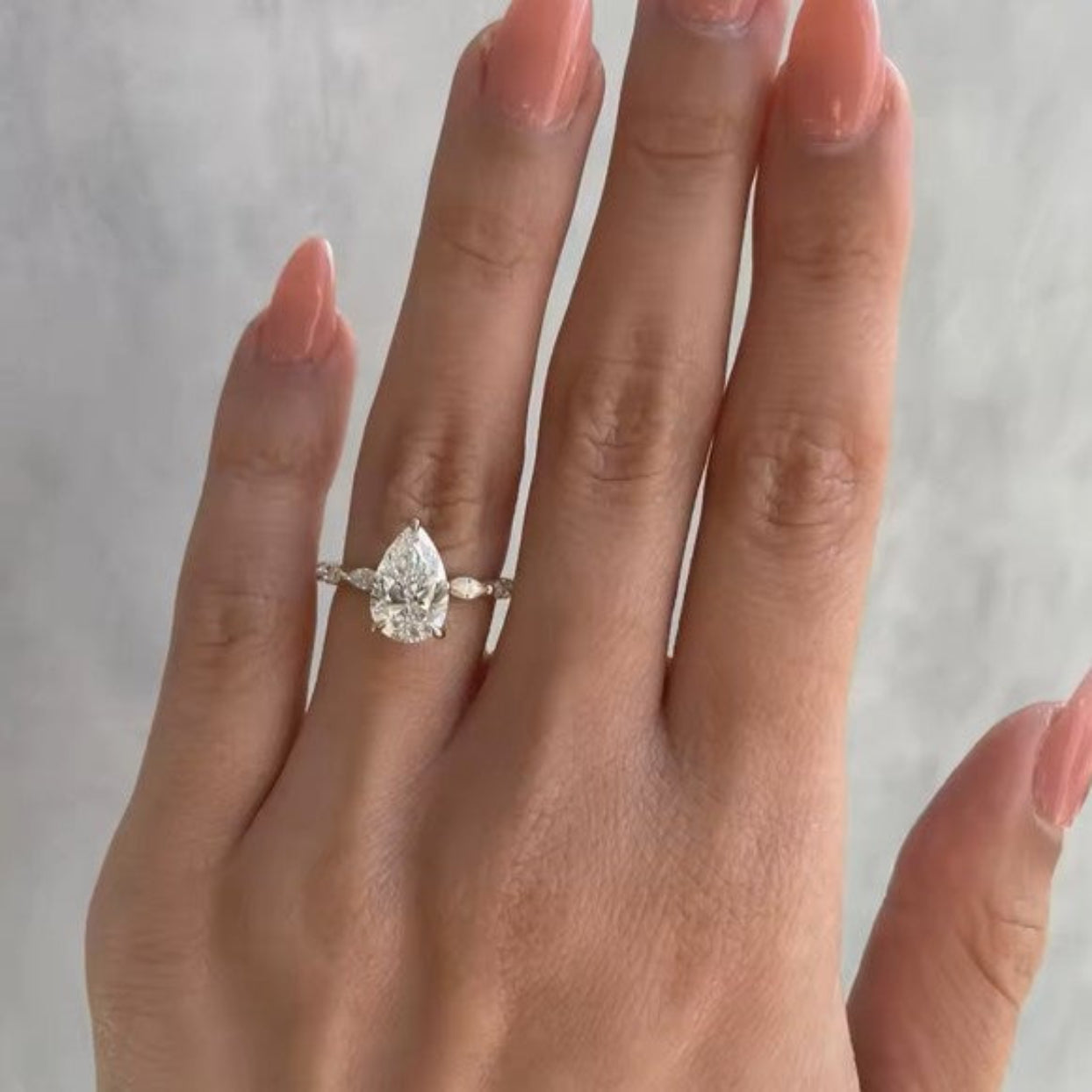 Hand wearing a pear-shaped diamond ring on a neutral background
