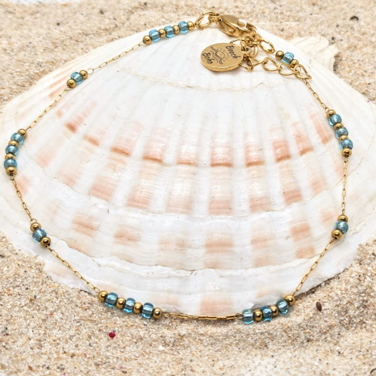Bracelet with blue and gold beads on a seashell on sand