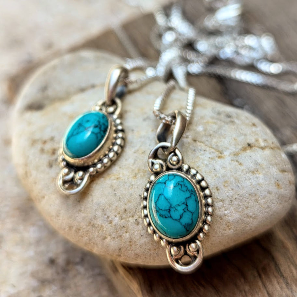 Turquoise stone pendants on silver chains resting on a rock.