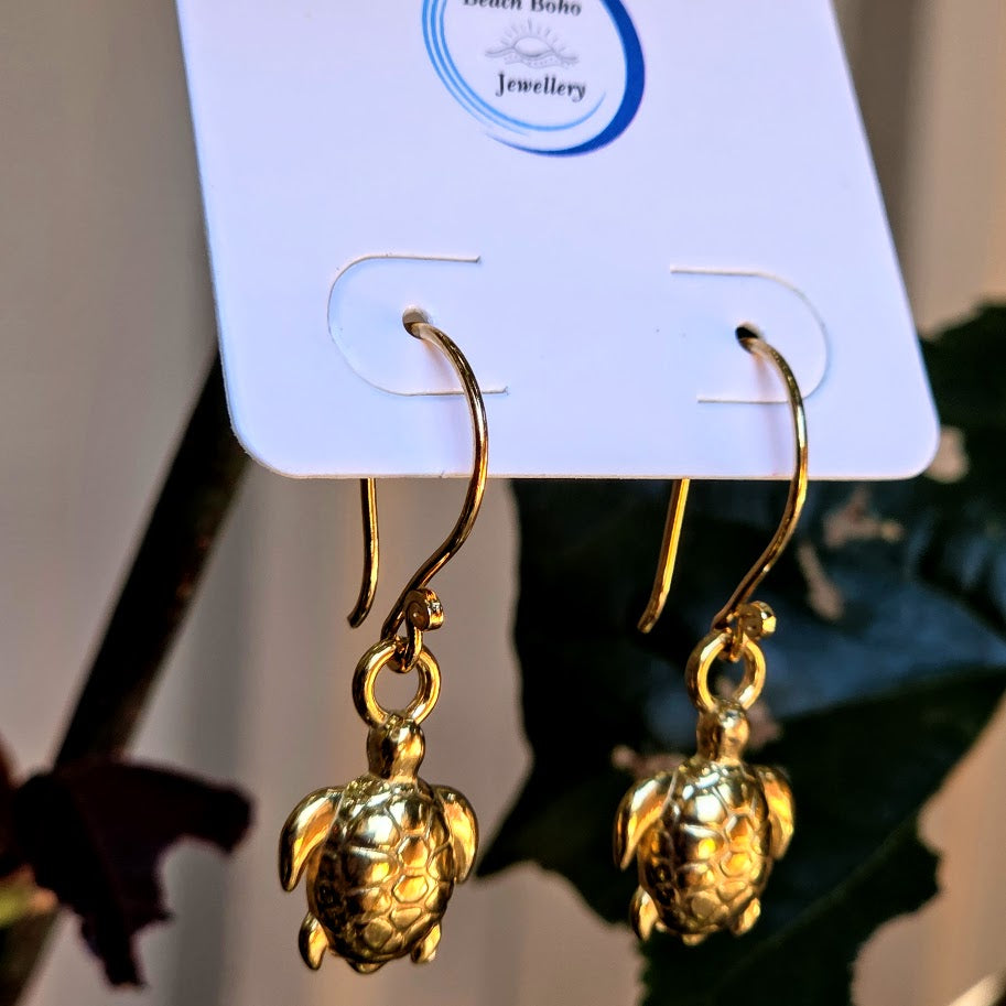 Gold turtle earrings on a branded card with a blurred background