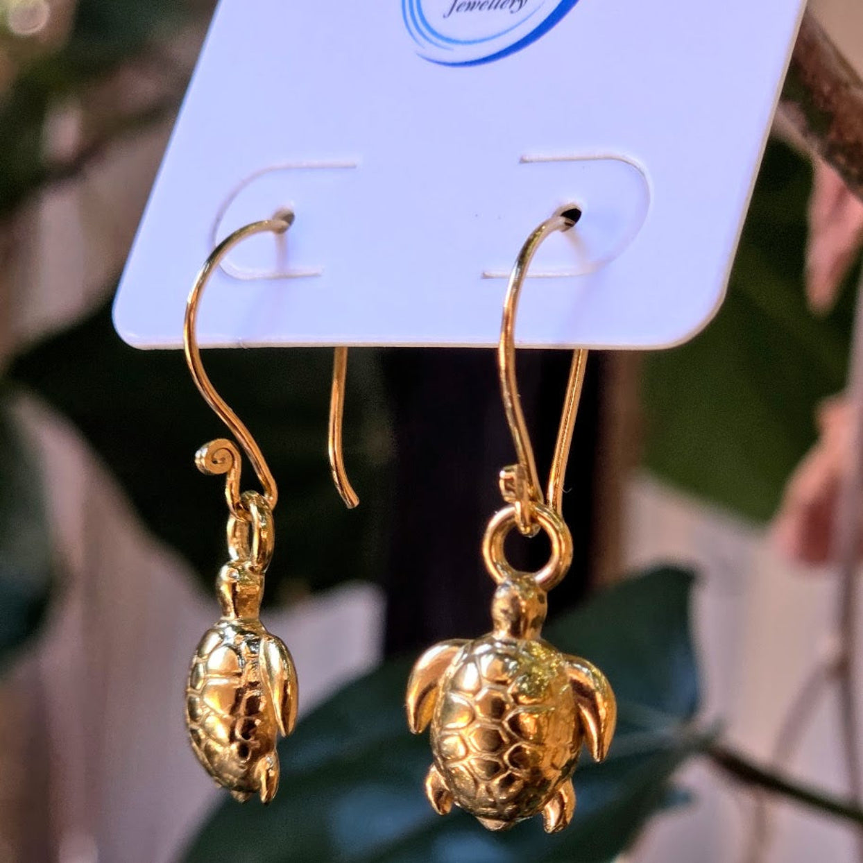 Gold turtle-shaped earrings on a display card with a blurred background