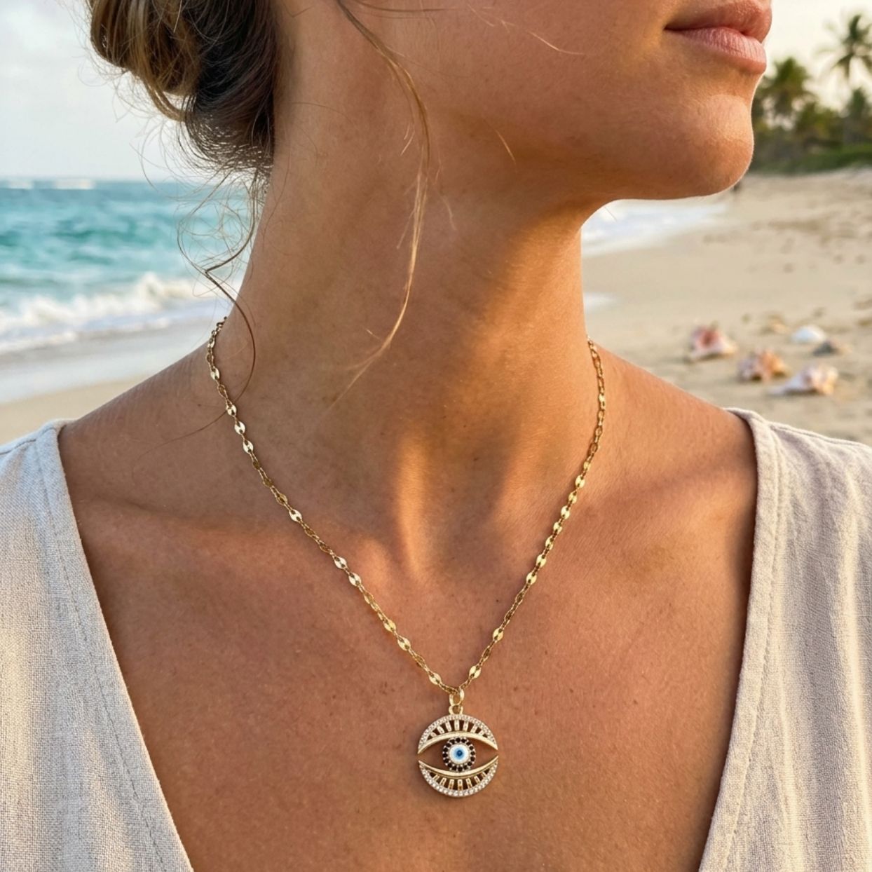 Woman wearing a gold necklace with an eye pendant on a beach