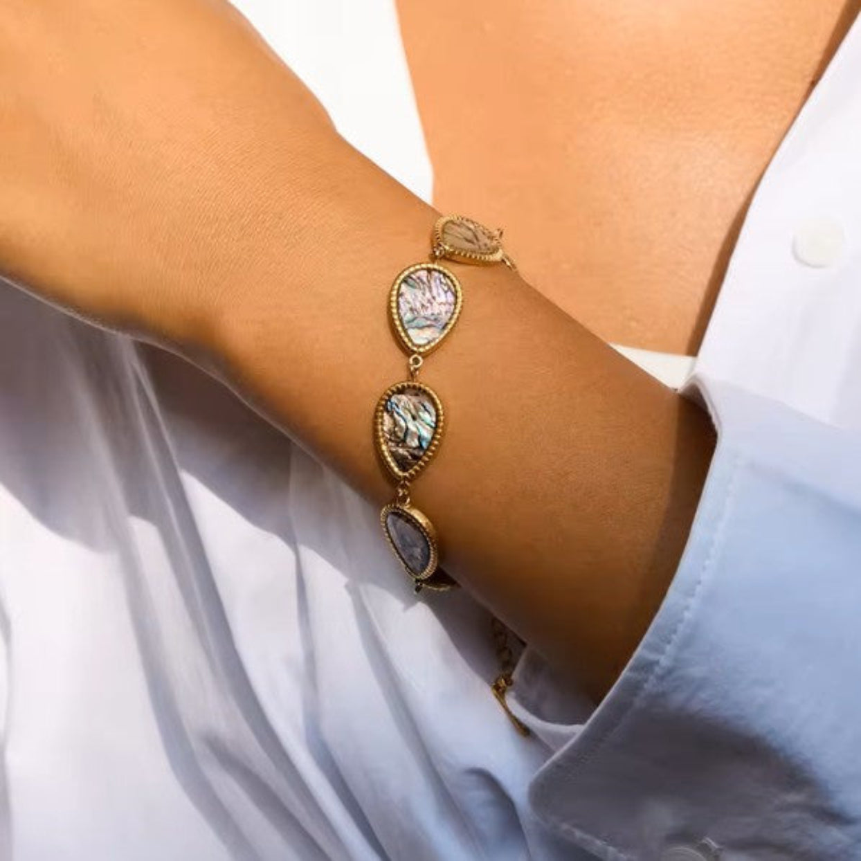 Gold bracelet with gemstones on a wrist against a white shirt background