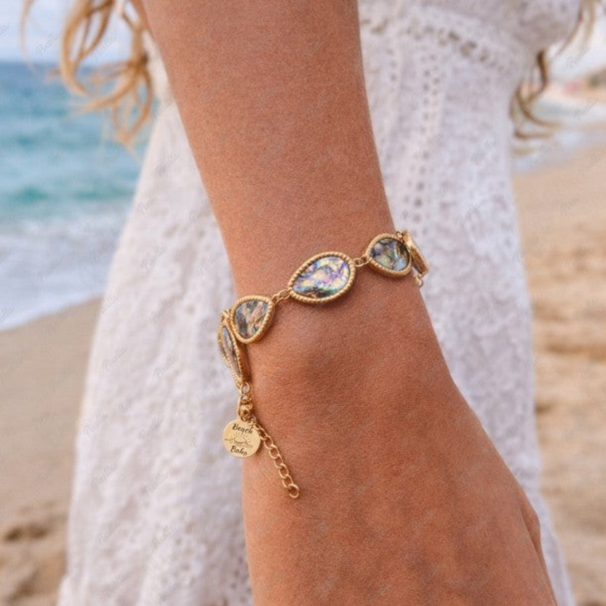 Gold bracelet with gemstones on a person's wrist by the beach