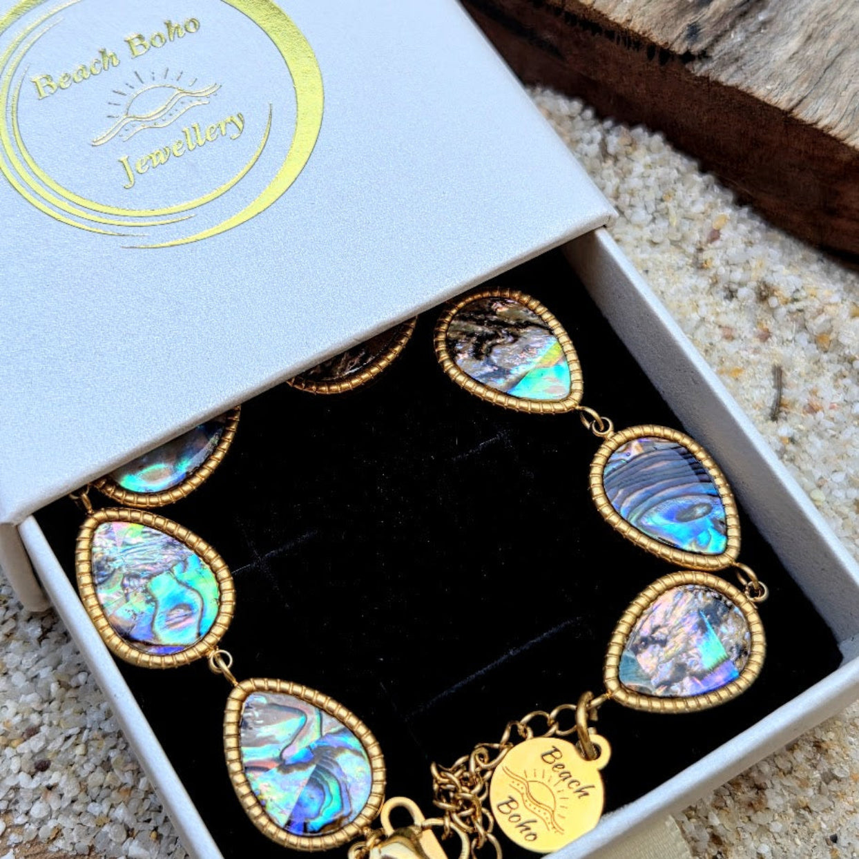 Jewelry box with a gold and abalone shell bracelet on a sandy background