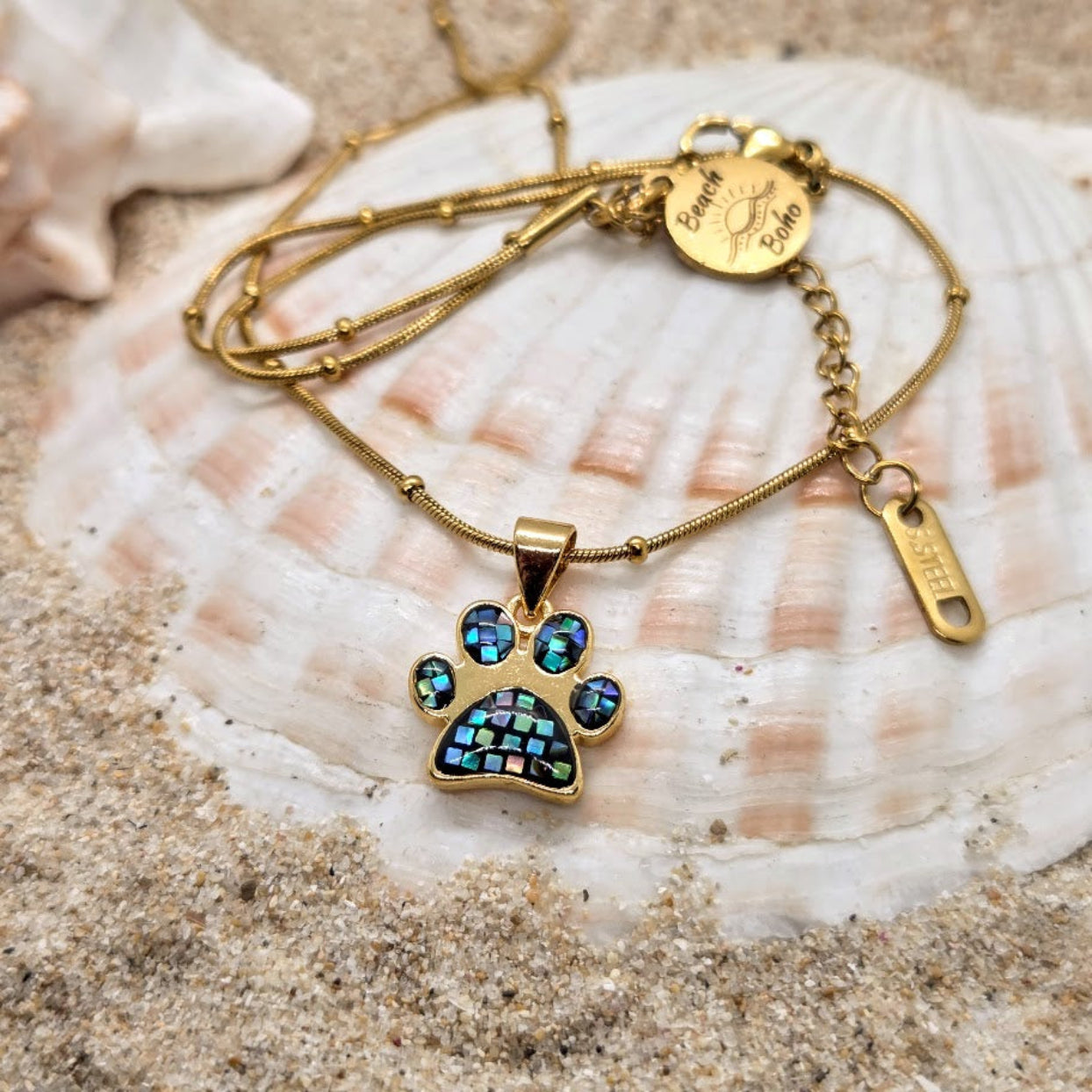 Gold bracelet with a paw-shaped pendant on a seashell