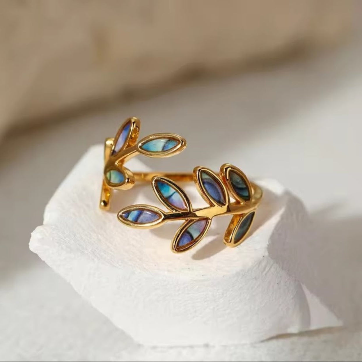 Gold leaf-shaped ring with blue gemstones on a white surface