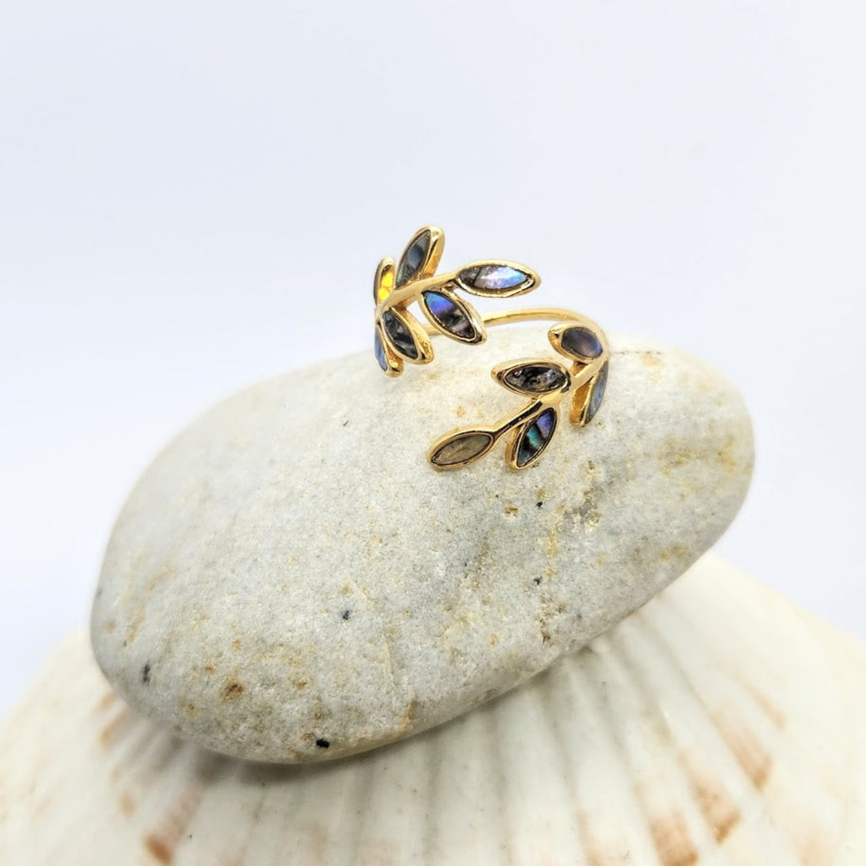 Gold leaf-shaped earring with gemstones on a stone surface