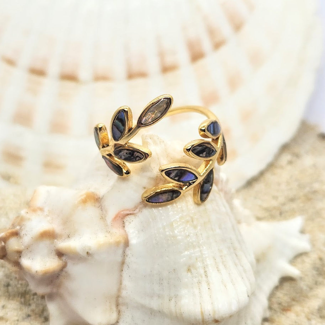 Gold leaf-shaped earring with purple stones on a seashell background