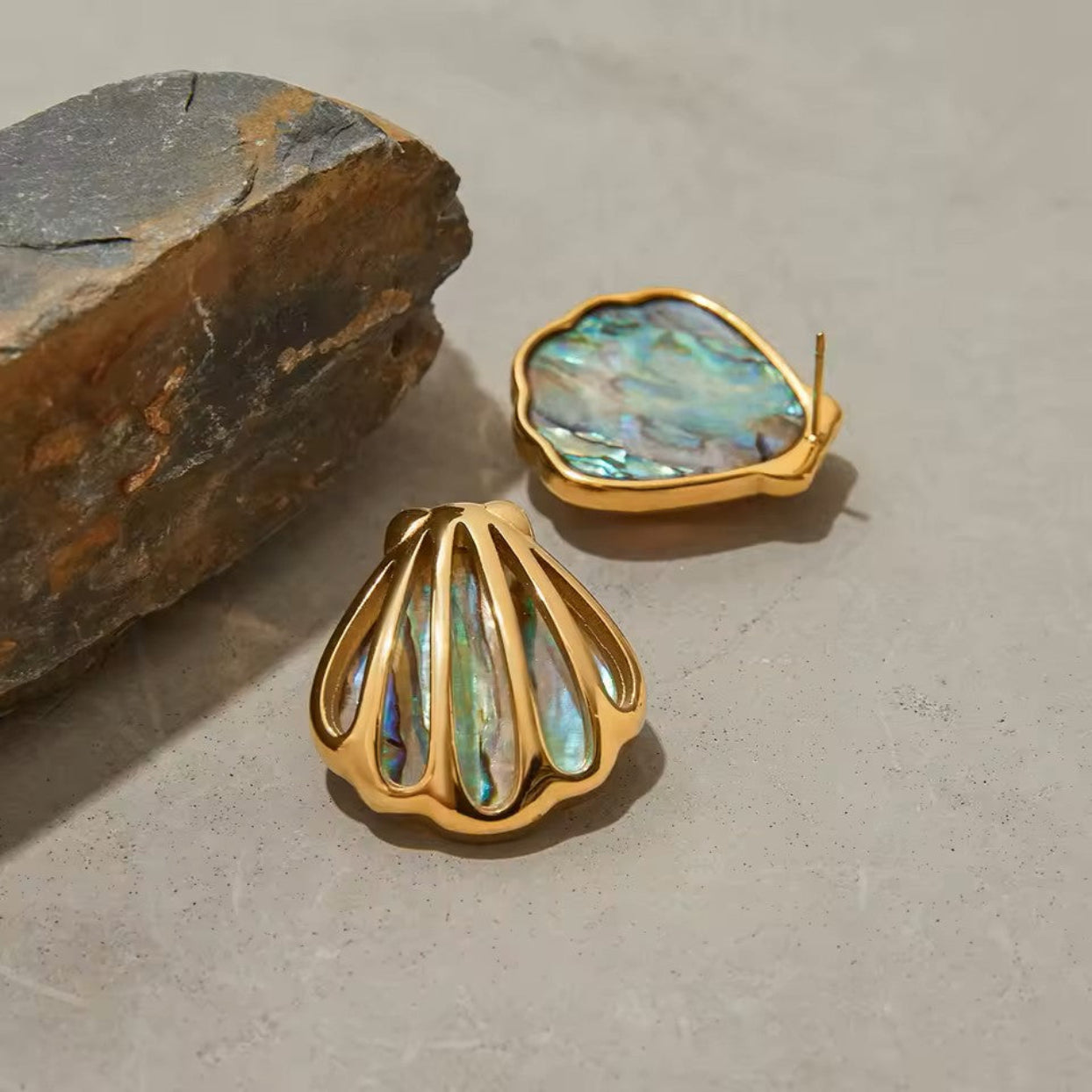 Gold earrings with multicolored stone inlays on a stone surface