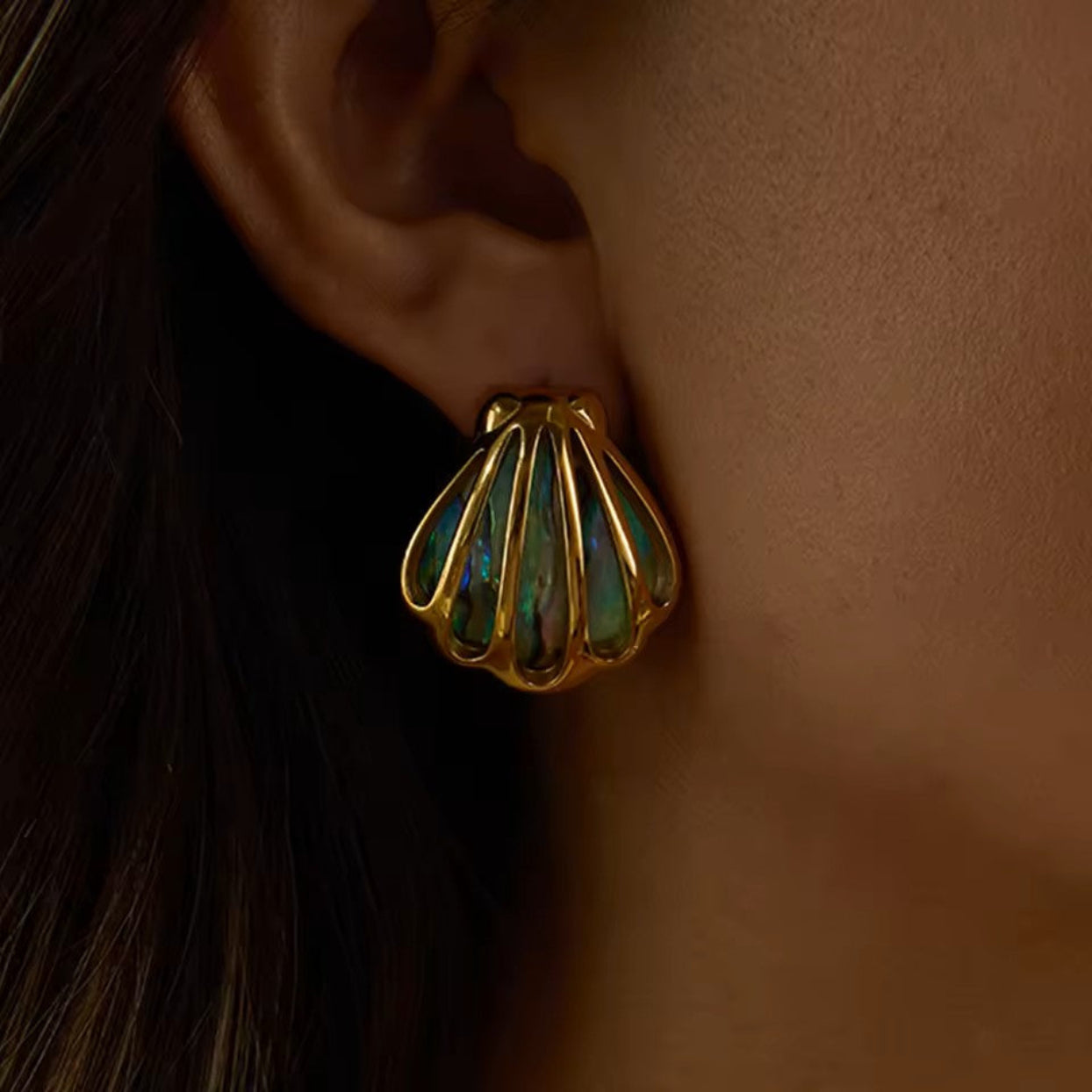 Gold shell-shaped earring with green gemstones worn by a person.