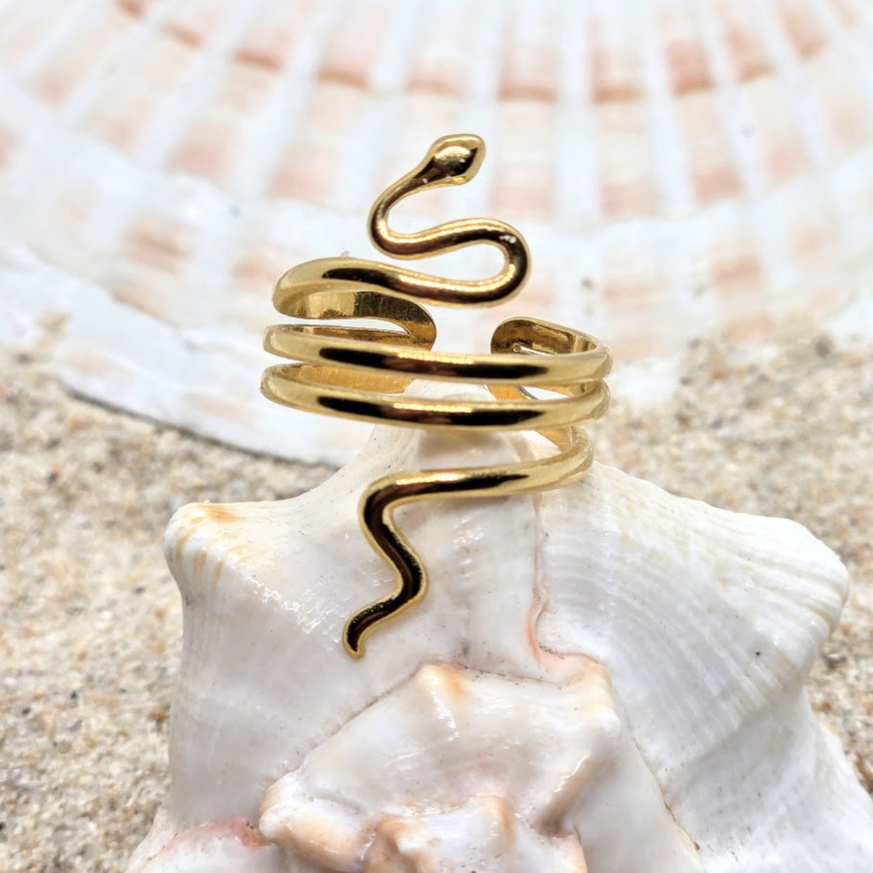 Gold snake-shaped ring on a seashell with a beach background