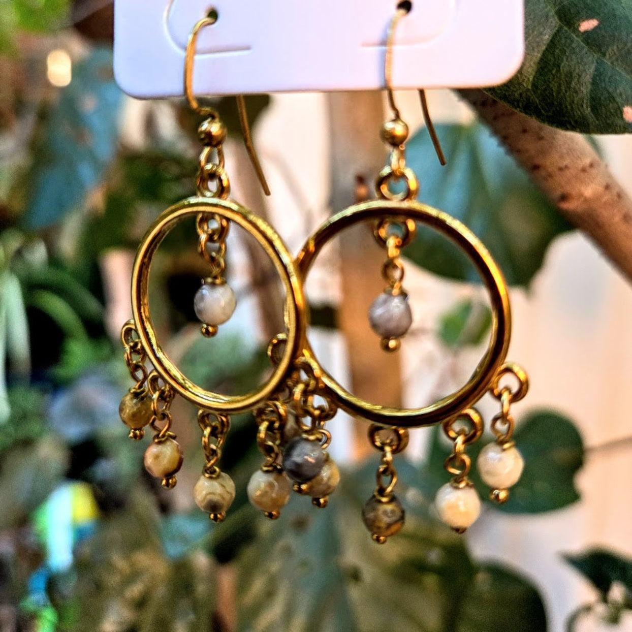 Gold hoop earrings with pearl-like beads hanging on a hook against a blurred natural background.