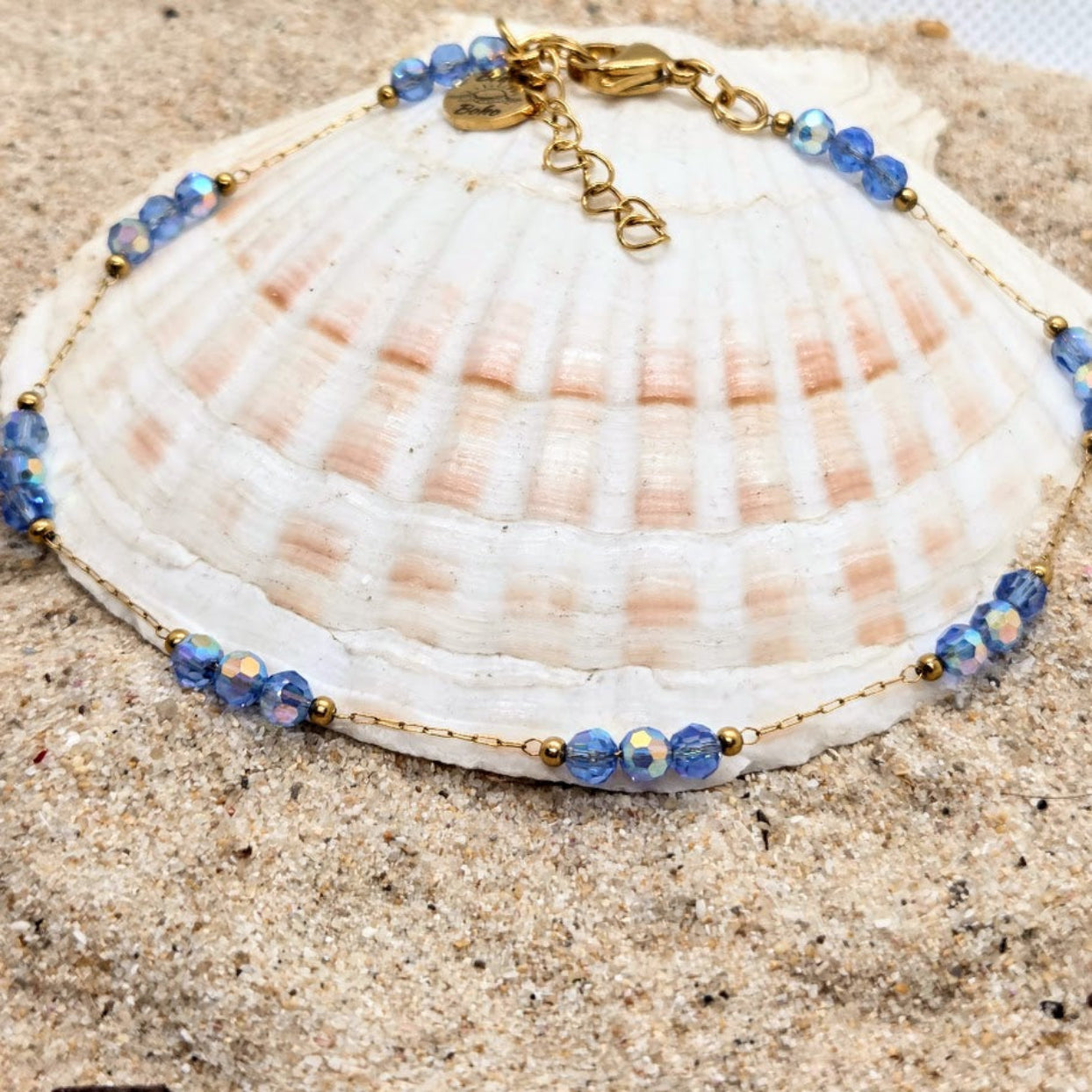Bracelet with blue beads and gold accents on a seashell against a sandy background