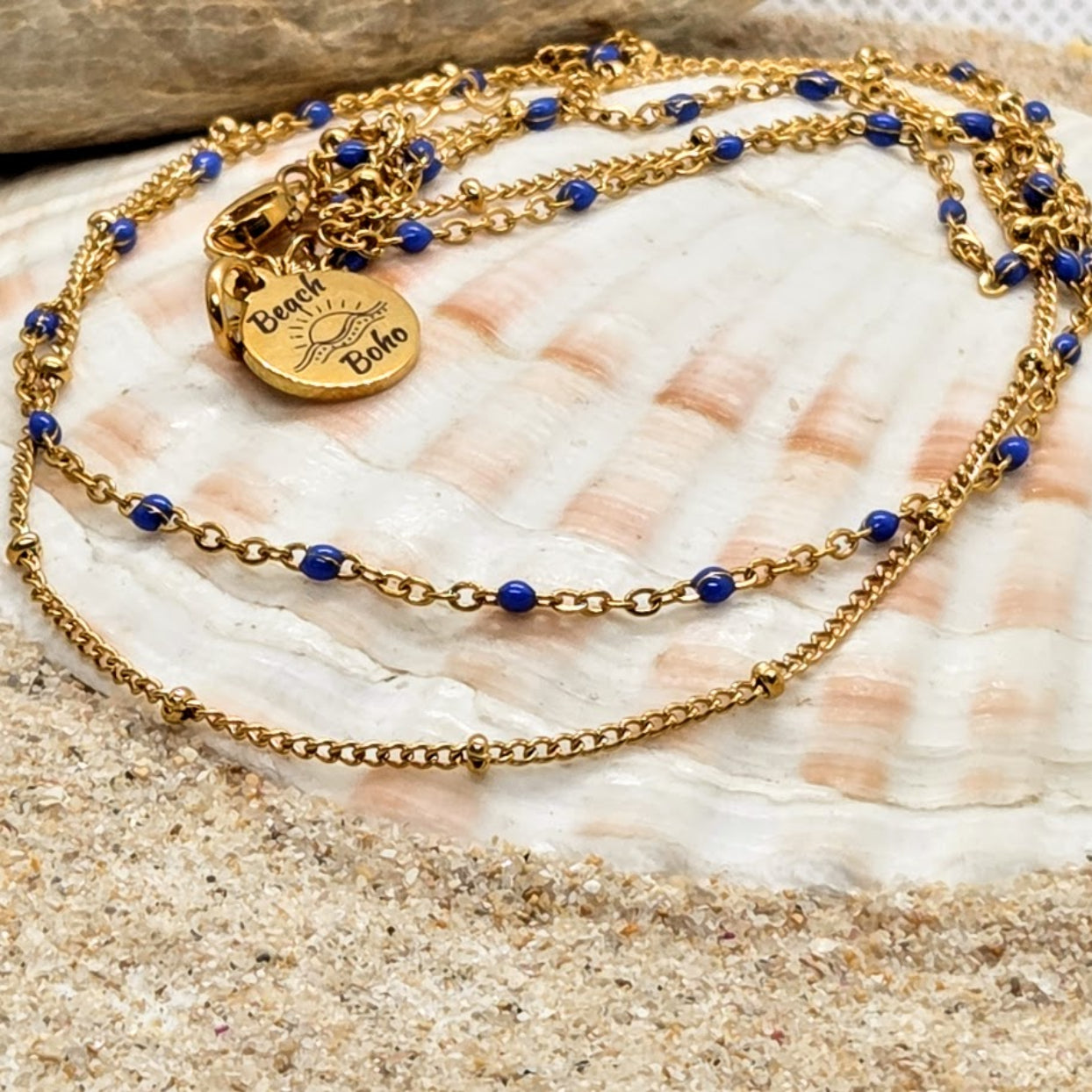Gold necklace with blue beads on a seashell with sand background