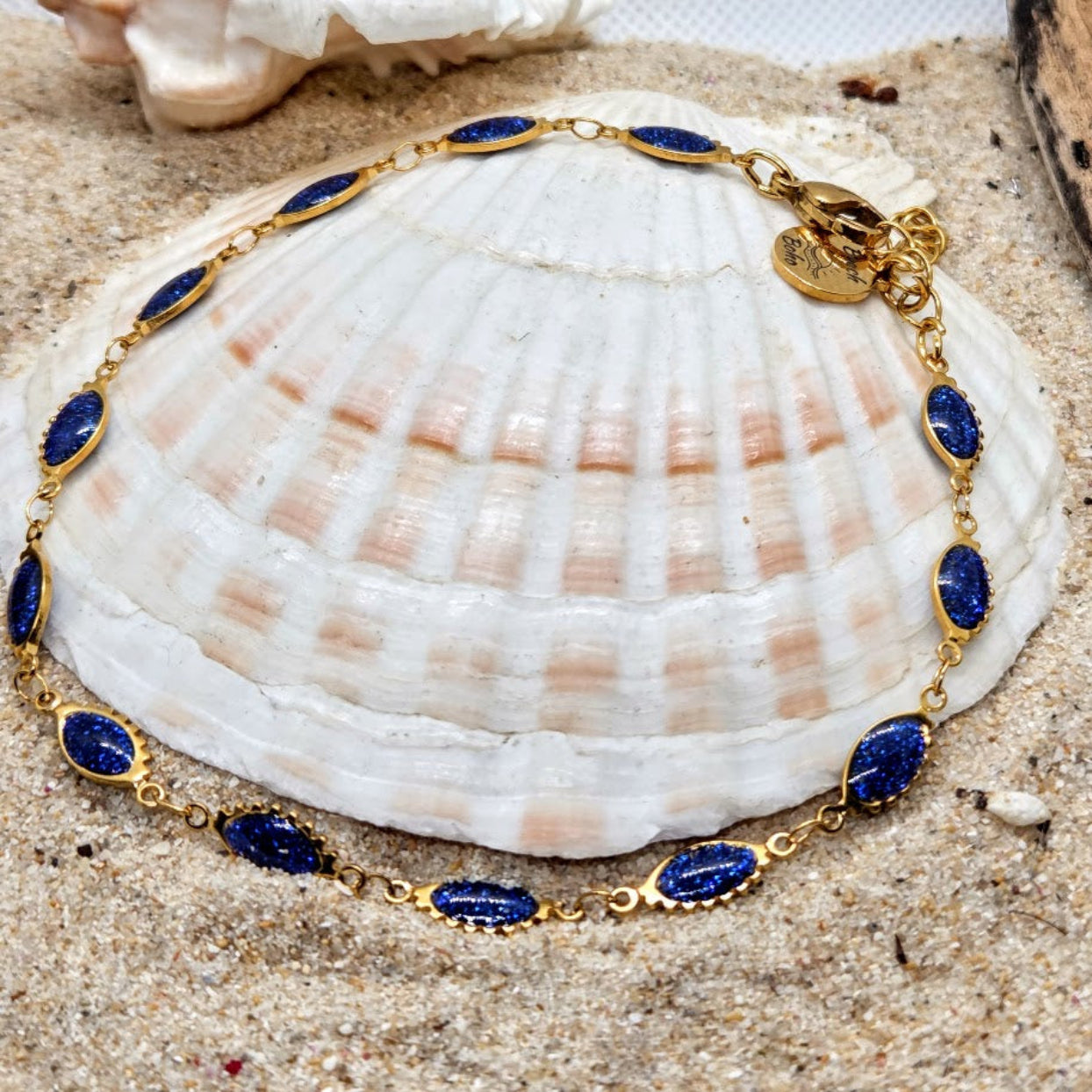 Gold bracelet with blue stones on a seashell in sand