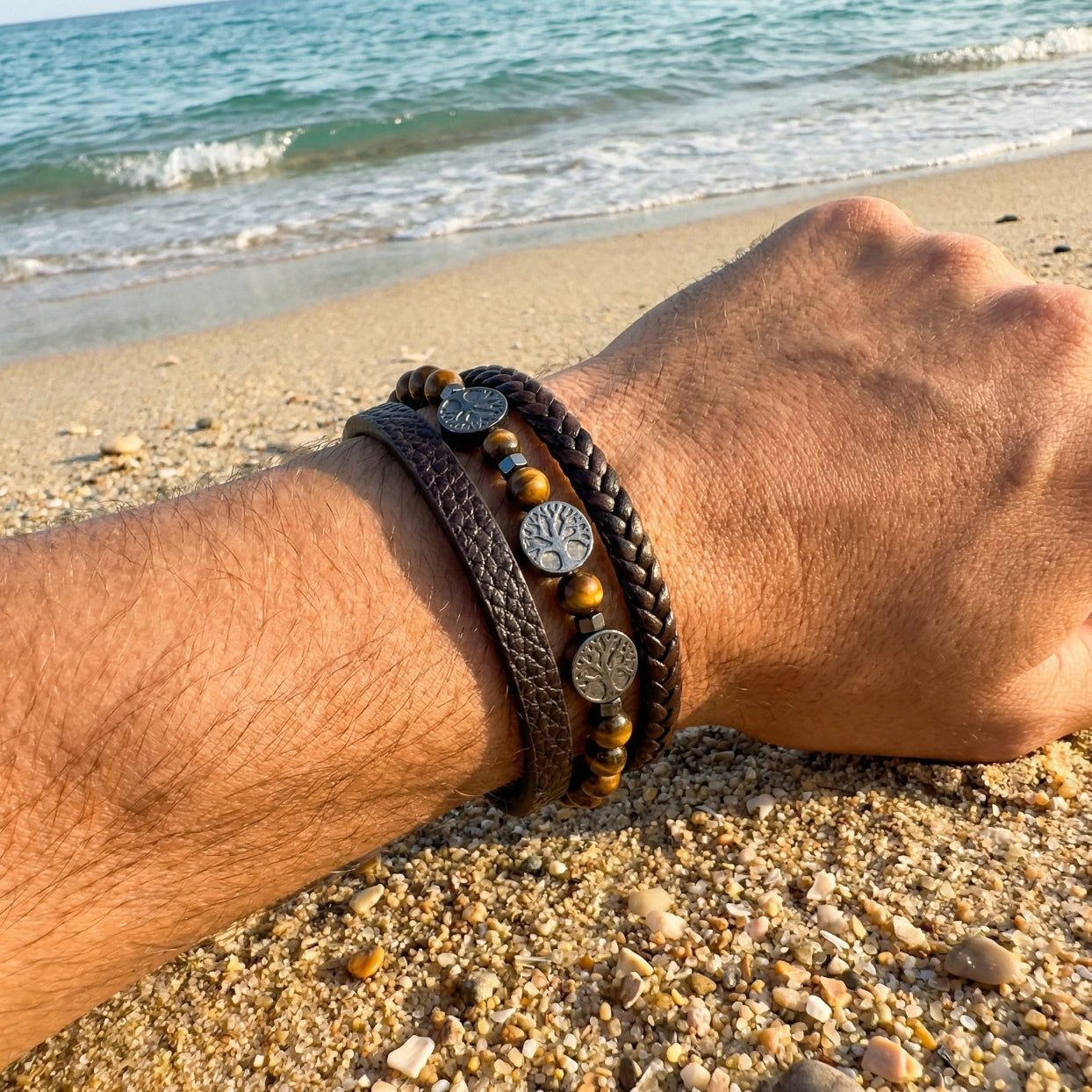 Wrist with braided bracelets on a sandy beach with ocean waves in the background