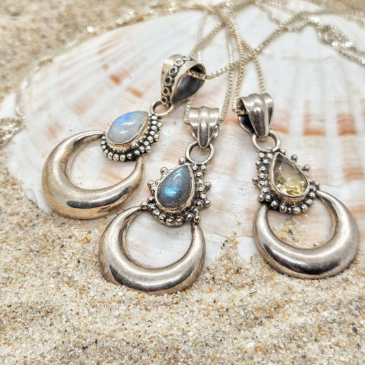 Silver pendants with gemstones on a shell and sand background