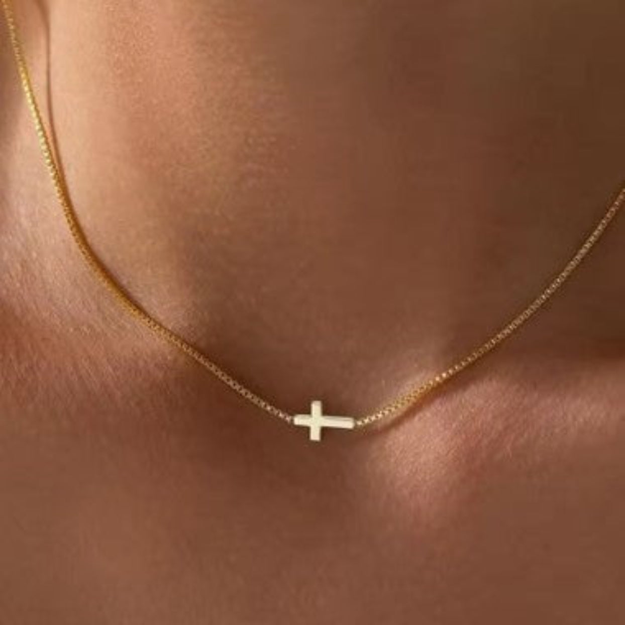 Gold necklace with a small cross pendant on a person's neck