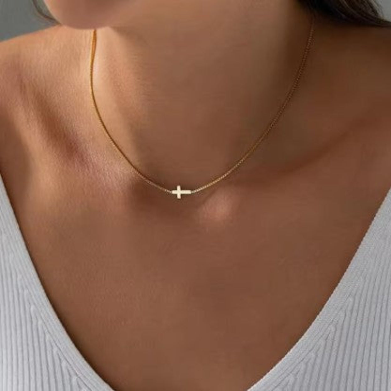 Gold necklace with a cross pendant worn by a person