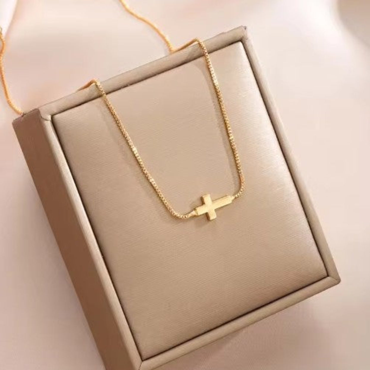 Gold necklace with a cross pendant on a beige jewelry box