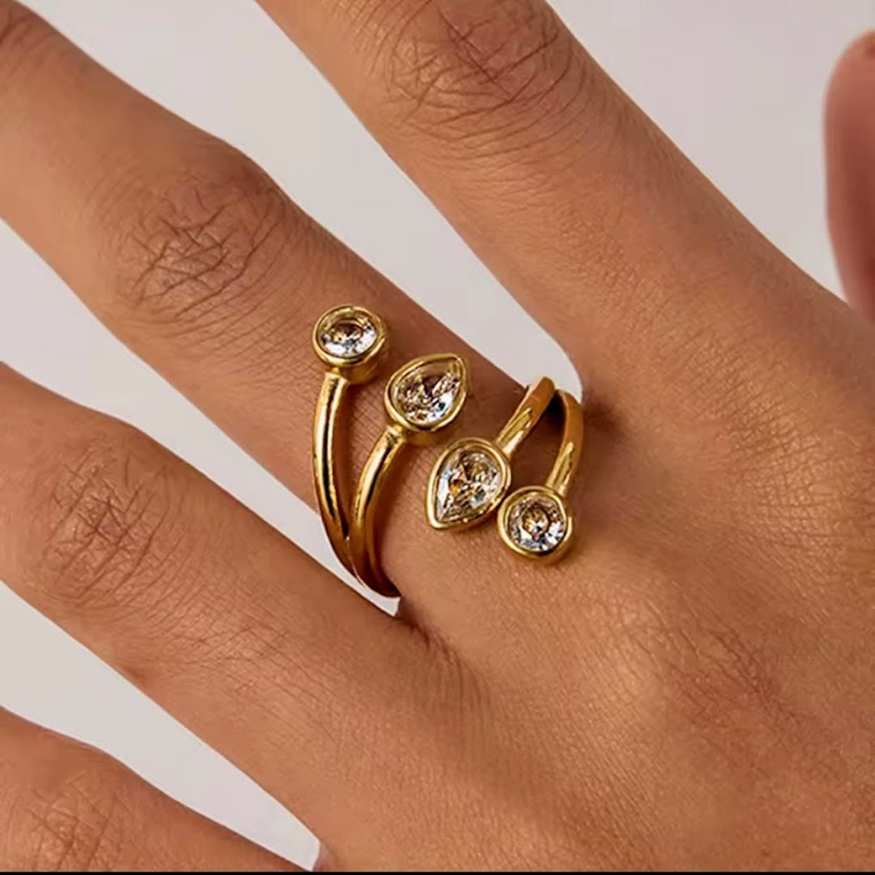 Gold ring with pear-shaped gemstones on a hand against a white background