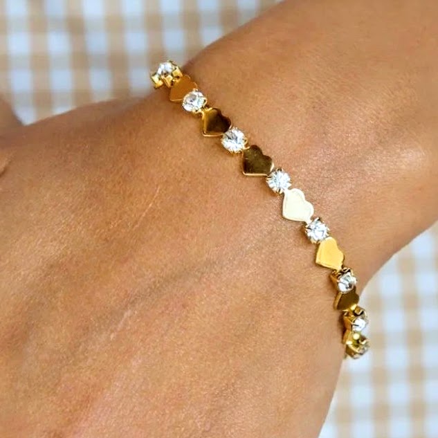 Gold and heart-shaped bracelet on a wrist with a blurred background