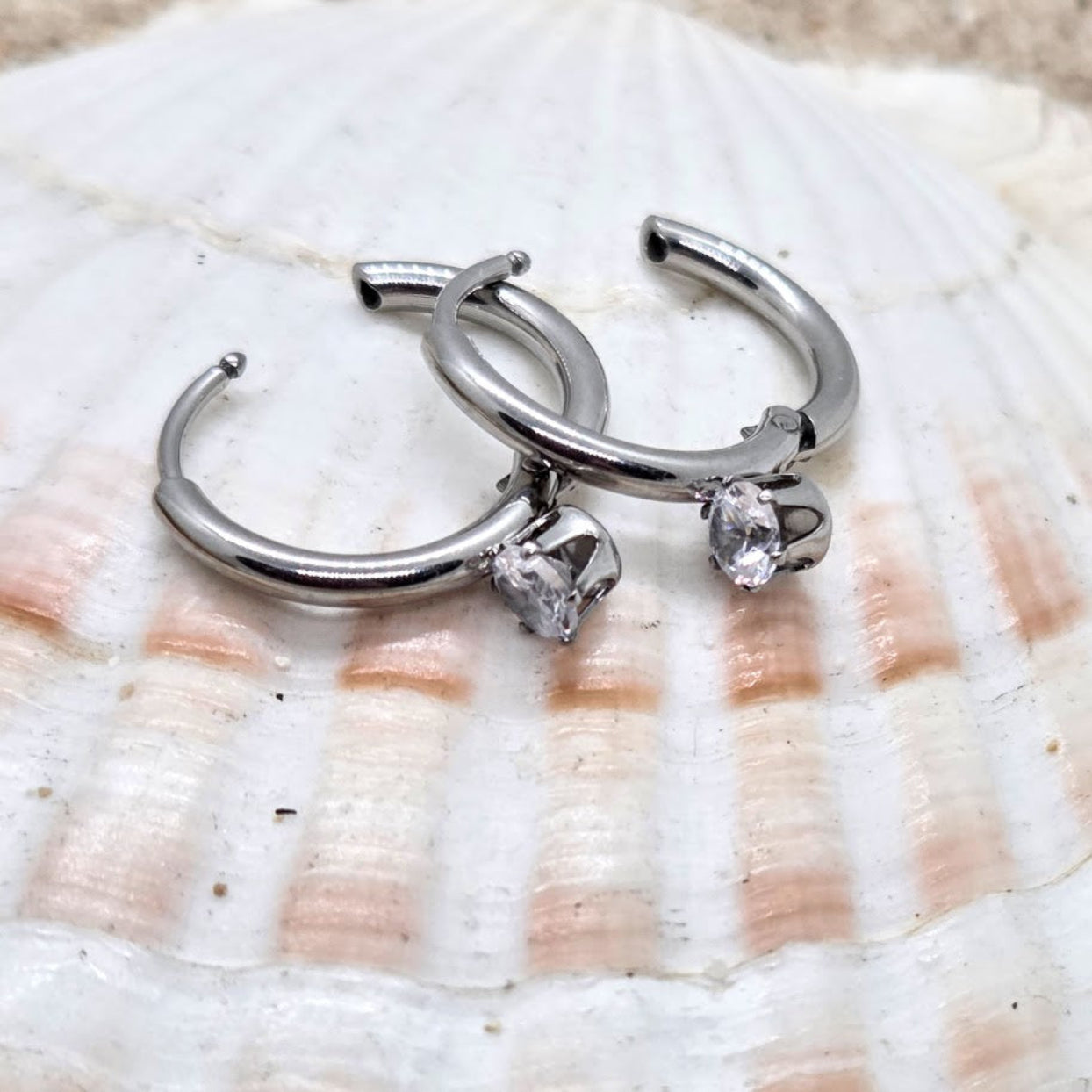 Silver hoop earrings with embedded stones on a shell background