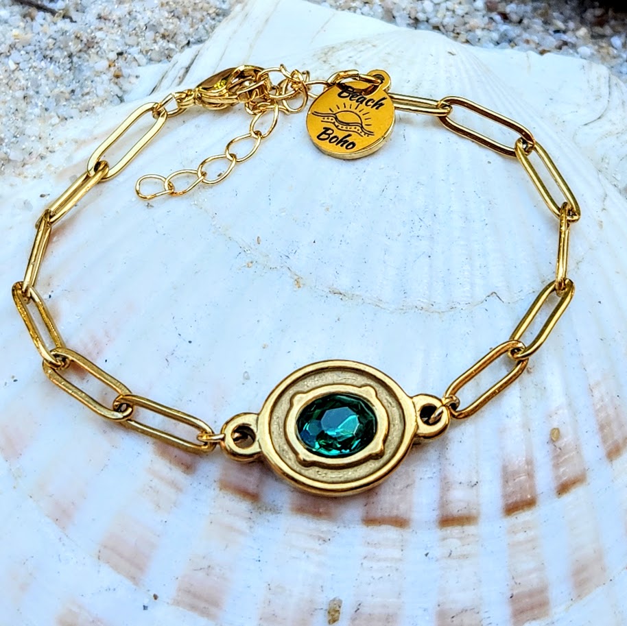Gold bracelet with a green gemstone on a seashell background