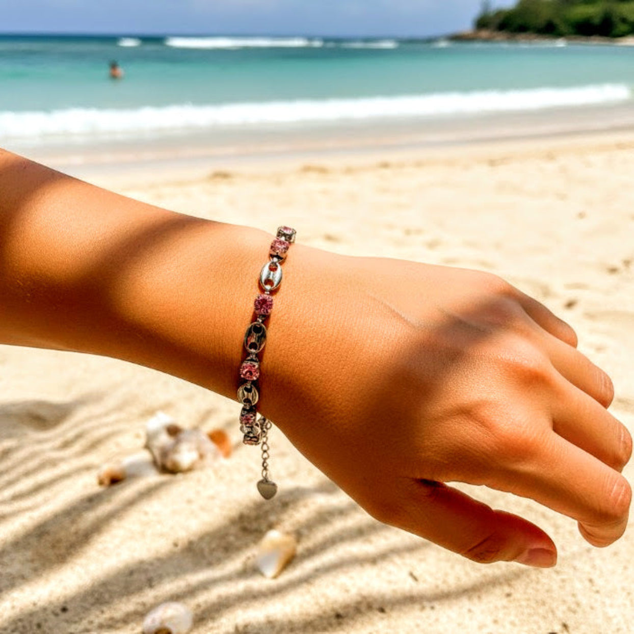 Hand wearing a bracelet on a sandy beach with ocean in the background