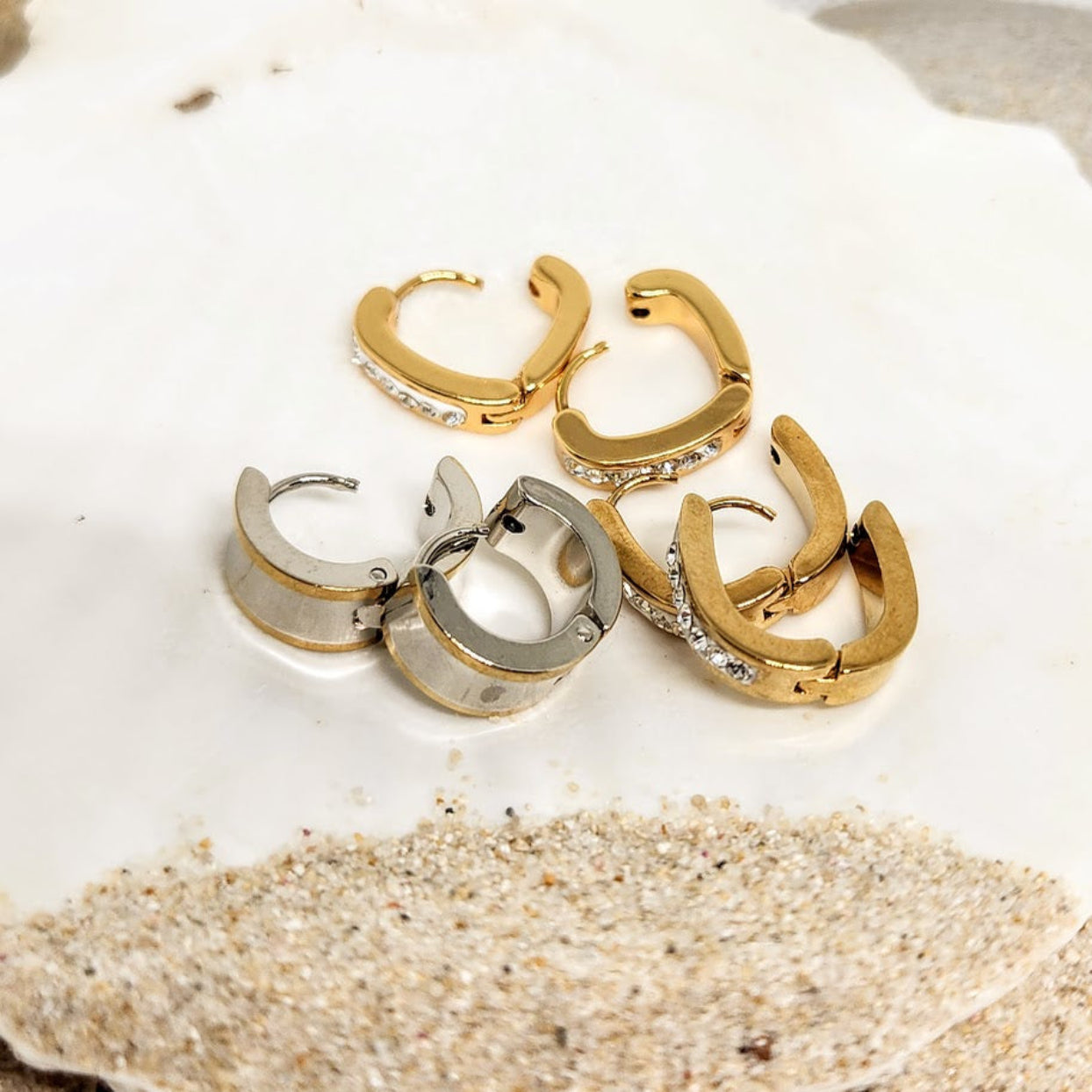 Three pairs of gold and silver hoop earrings on a textured white surface.