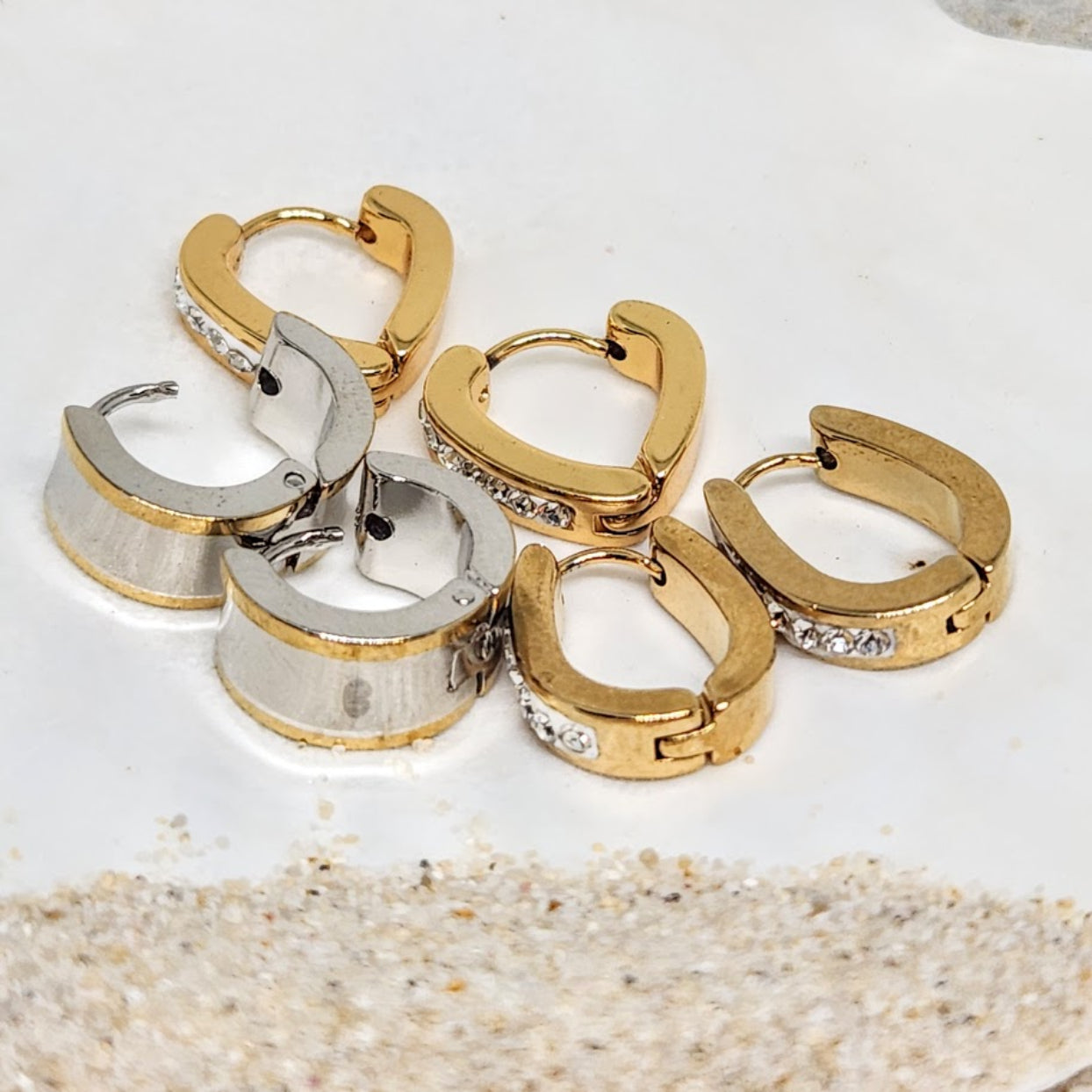 Gold and silver hoop earrings on a textured surface