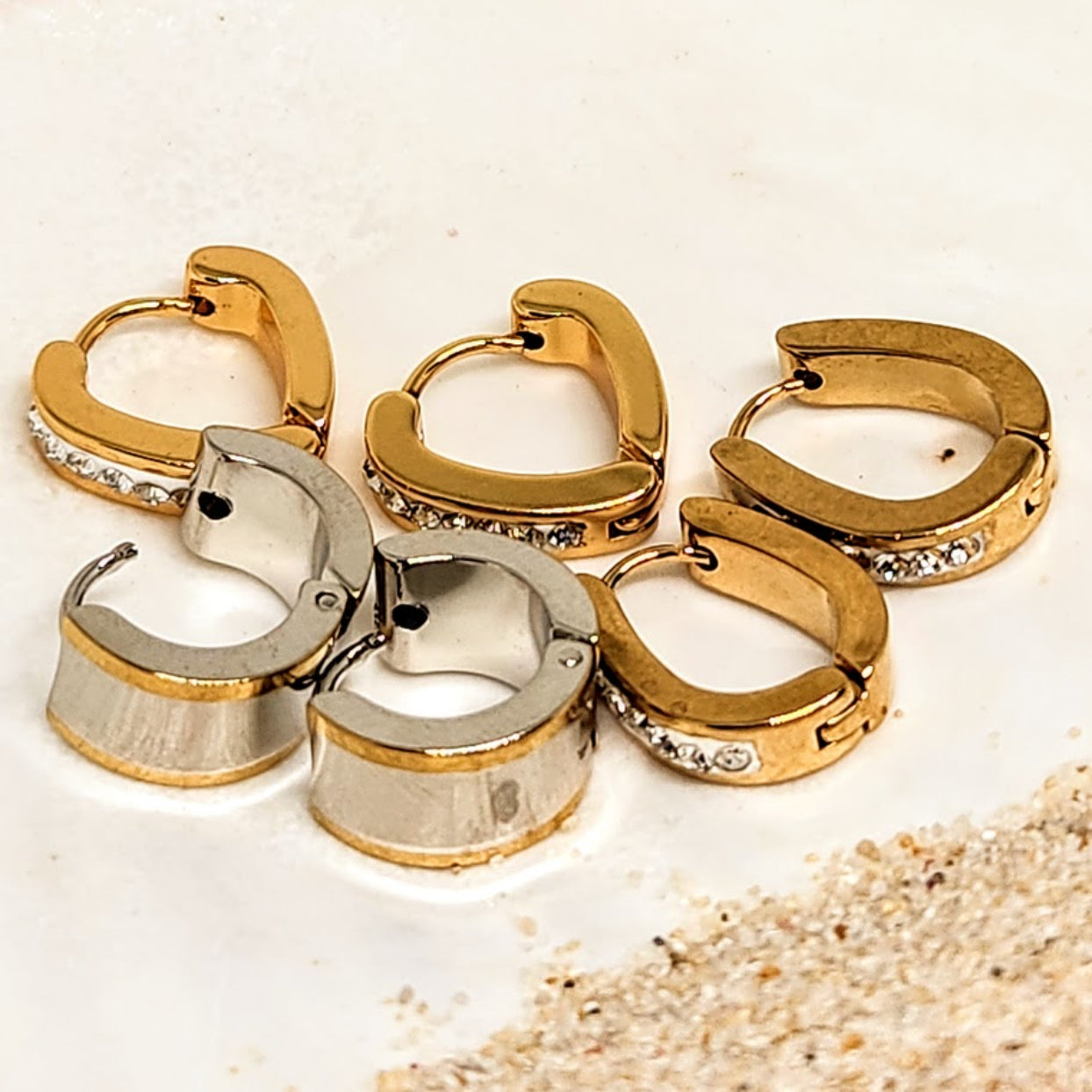 Gold and silver hoop earrings on a textured beige surface