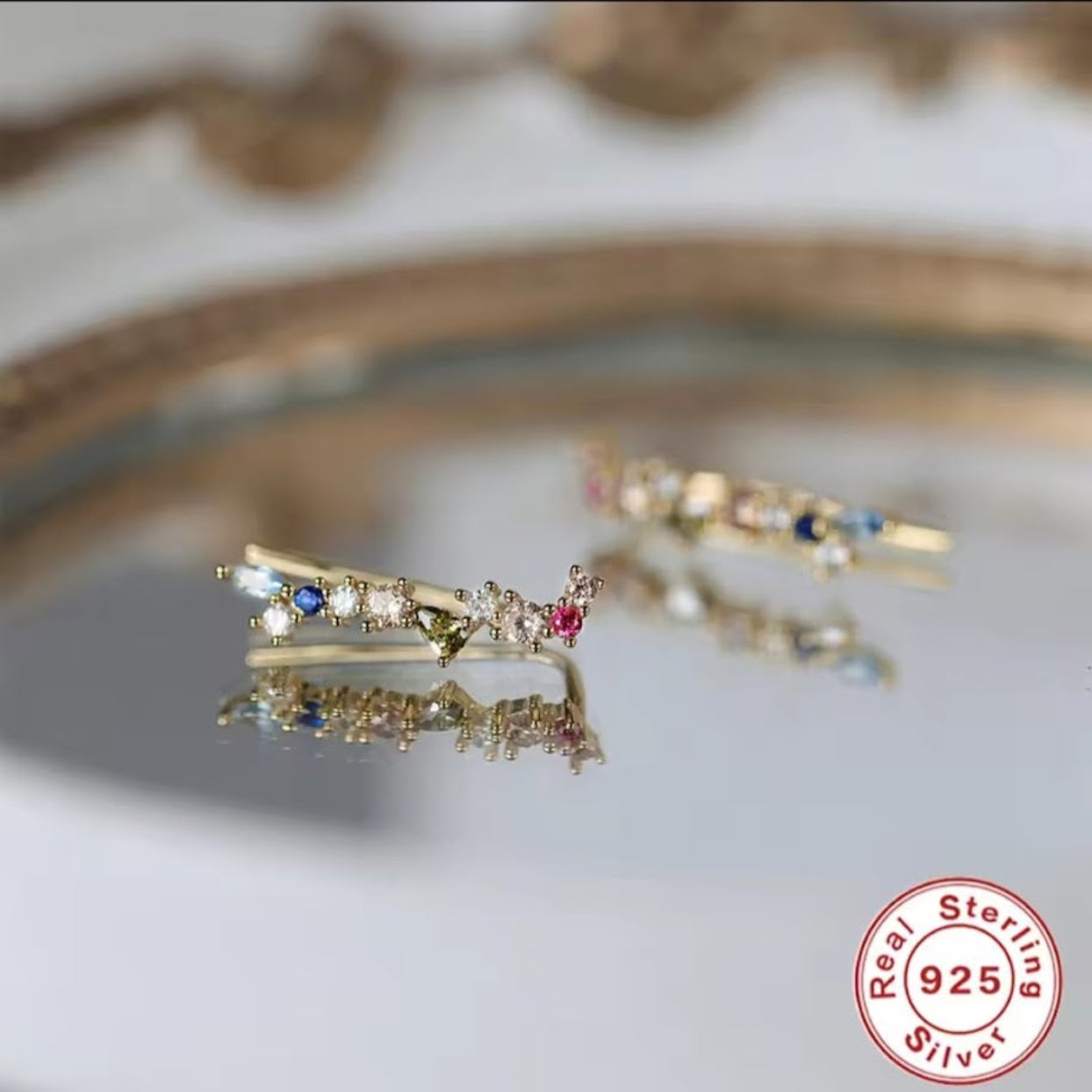 Gold ring with gemstones on a reflective surface, featuring a 'Real Sterling Silver 925' stamp.