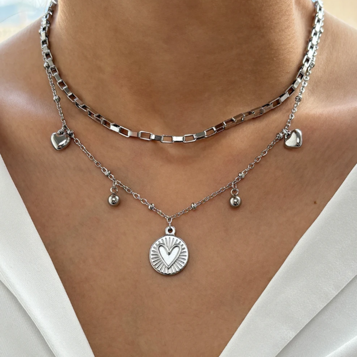 Silver necklace with heart pendants on a person wearing a white top.
