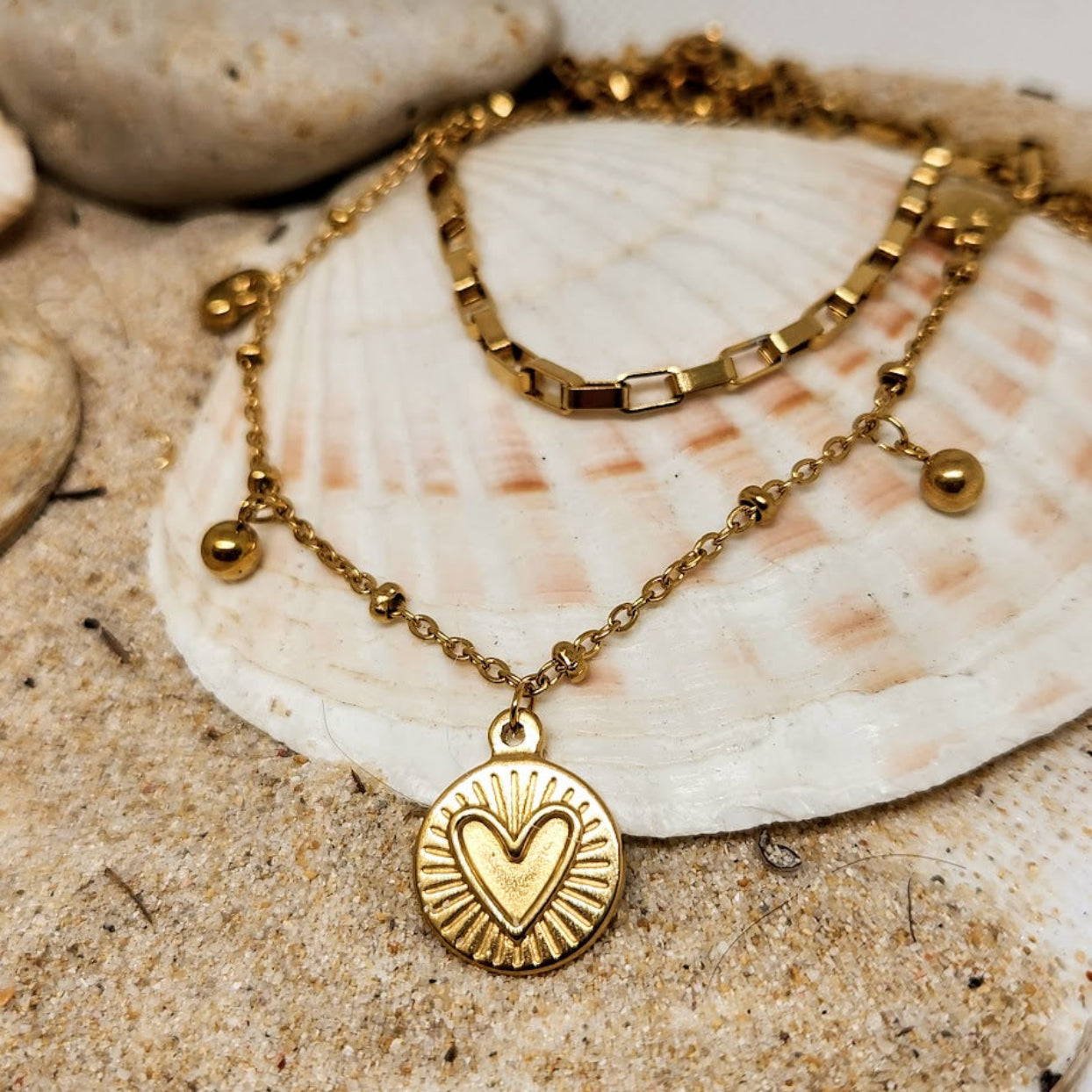 Gold necklace with a heart pendant on a seashell in sand