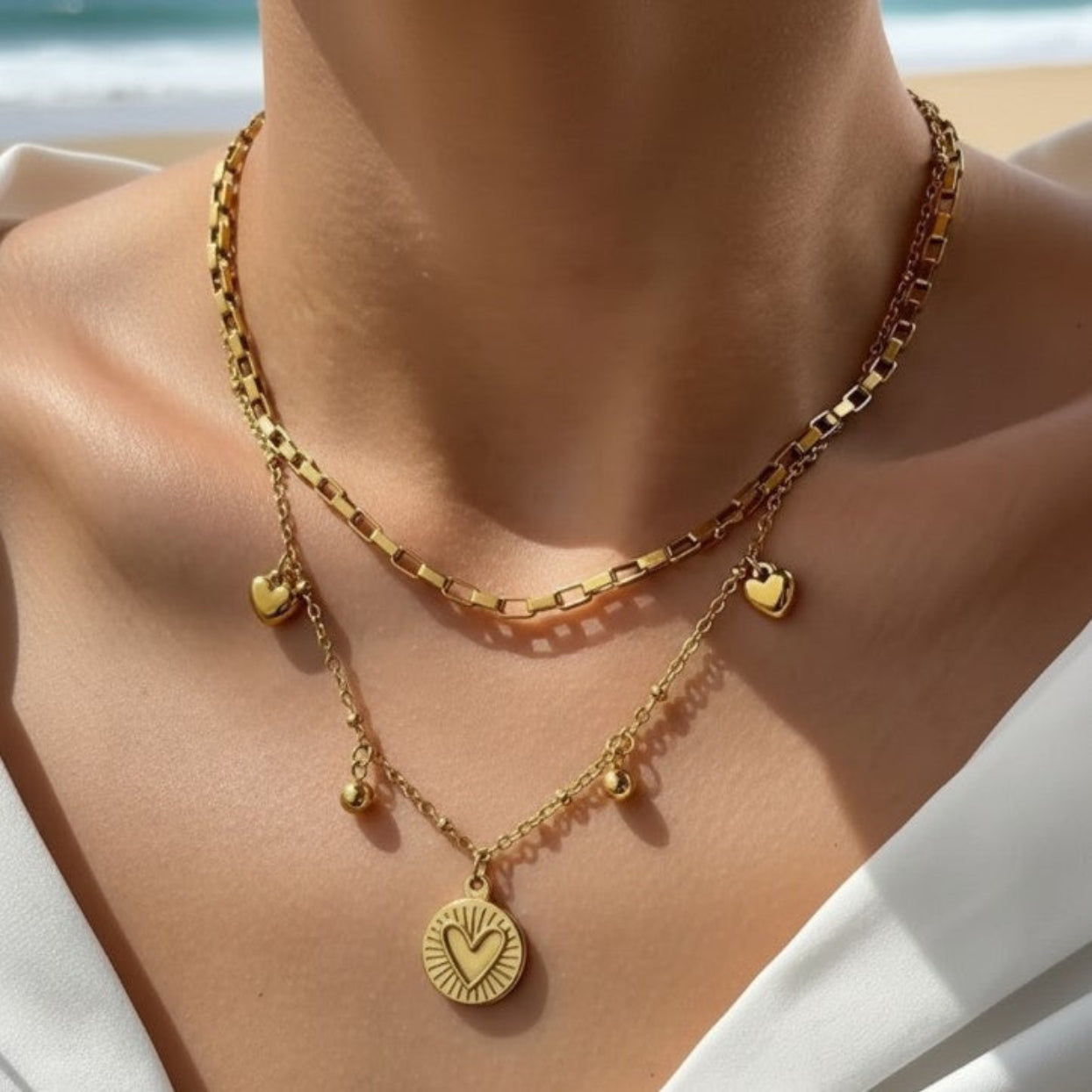 Gold necklace with heart and round pendants on a person against a beach background
