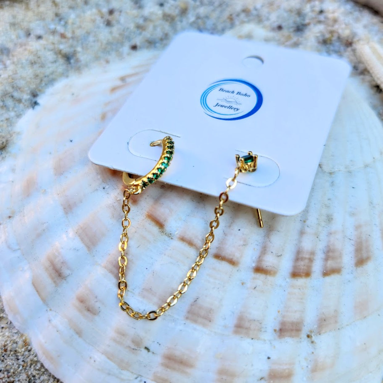 Gold chain earrings on a card with a shell background