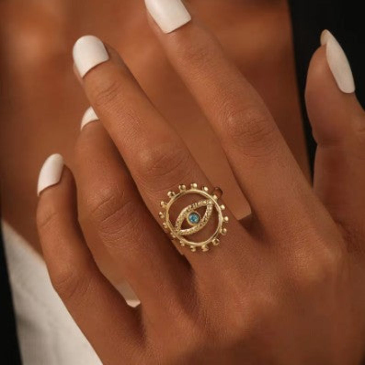 Gold ring with a blue gemstone on a person's finger with white nail polish.