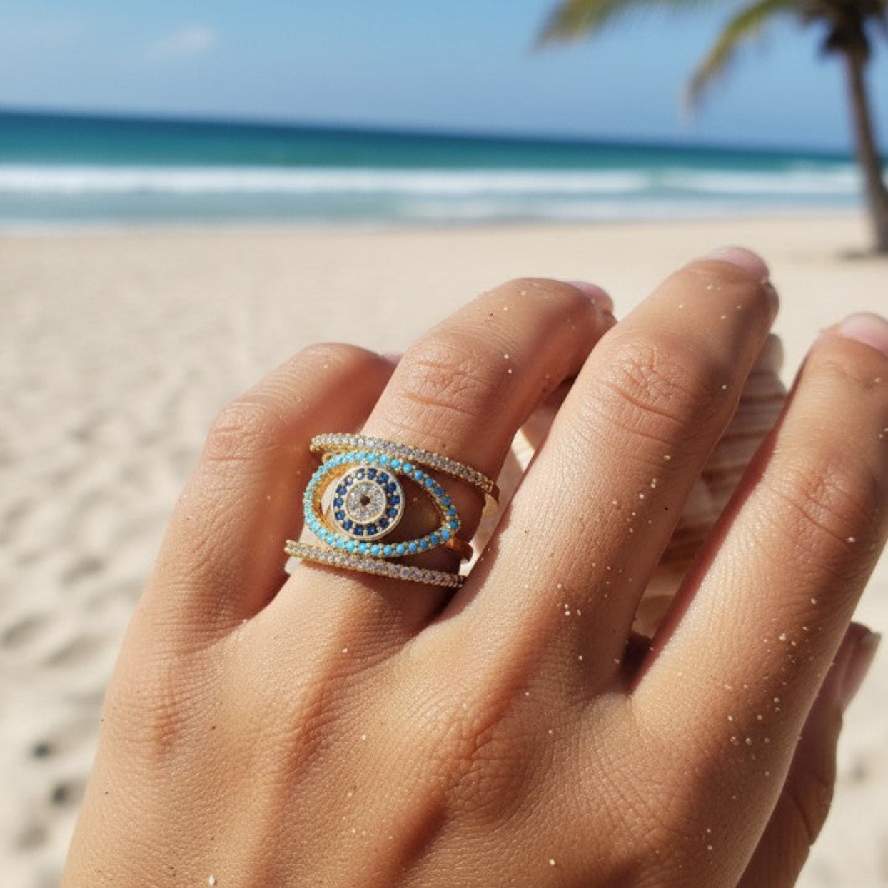 Hand wearing a decorative ring with a beach and palm tree in the background