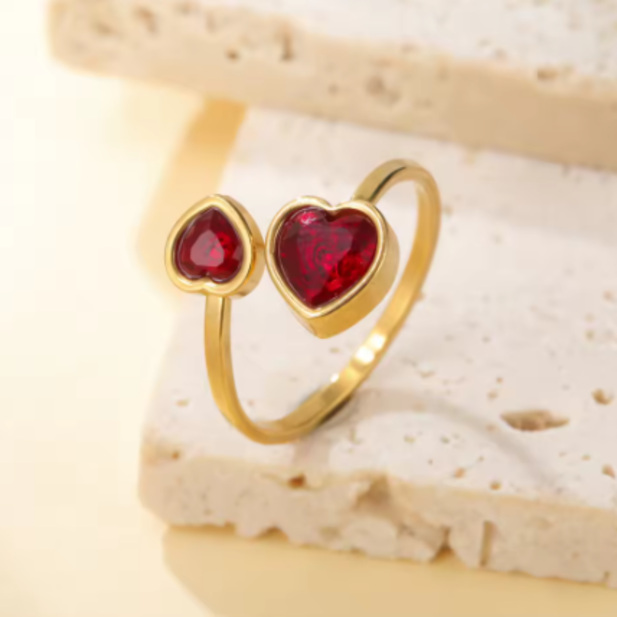 Gold ring with red heart-shaped stones on a textured beige surface
