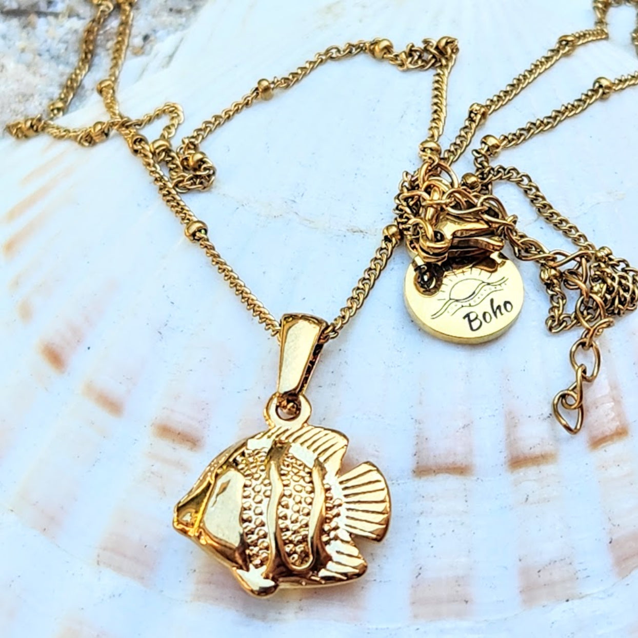 Gold fish pendant necklace with 'Boho' charm on a shell background