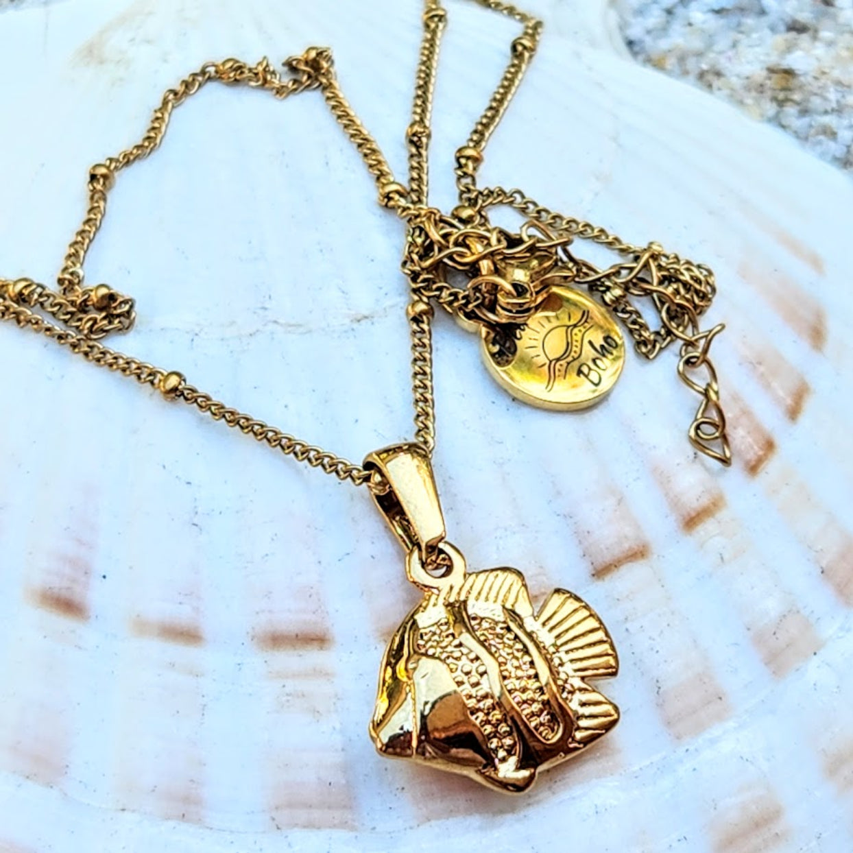 Gold fish pendant necklace on a shell background
